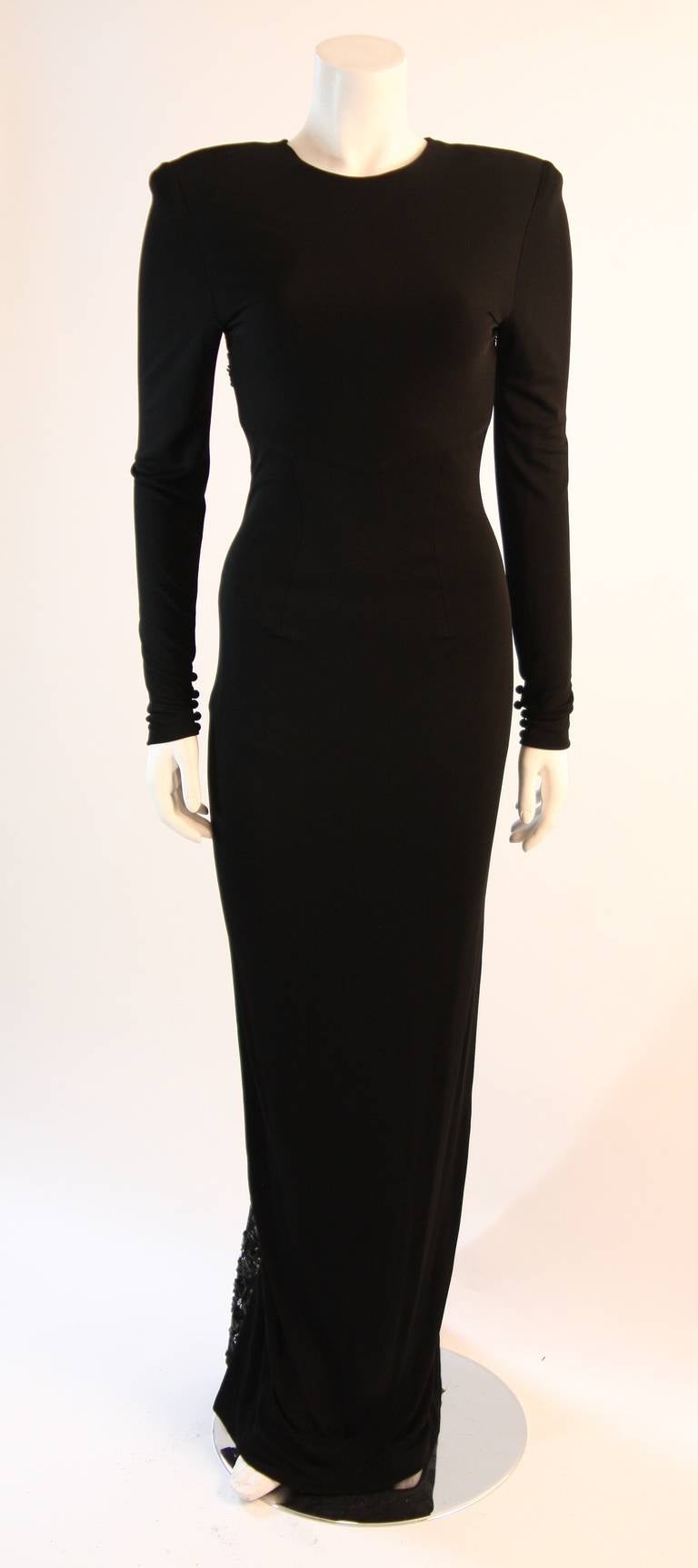 This is a superb Vicky Tiel gown. This gown is composed of a black stretch jersey and features an embellished lace back with the perfect amount of exposure, a stunning contrast to the sleek high neckline and long sleeves. Cascading just behind the