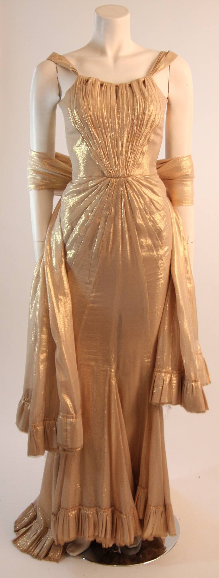 Dieses exquisite Kleid aus feinstem Goldseiden-Lamé präsentiert eine wunderschöne, körperumspielende Silhouette mit ausgestelltem Saum. Das Mieder in der vorderen Mitte ist mit handgefertigten Details versehen. 

Dies ist eine Couture-Bestellung