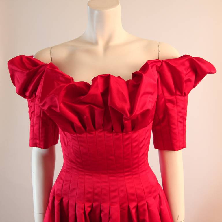 This is a stunning Nolan Miller design. The gown is composed of a beautiful cardinal red silk. The vibrant red silk is complimented by the crafted design of the tufted neckline. The wonderful off the shoulder neckline offers the perfect balance to