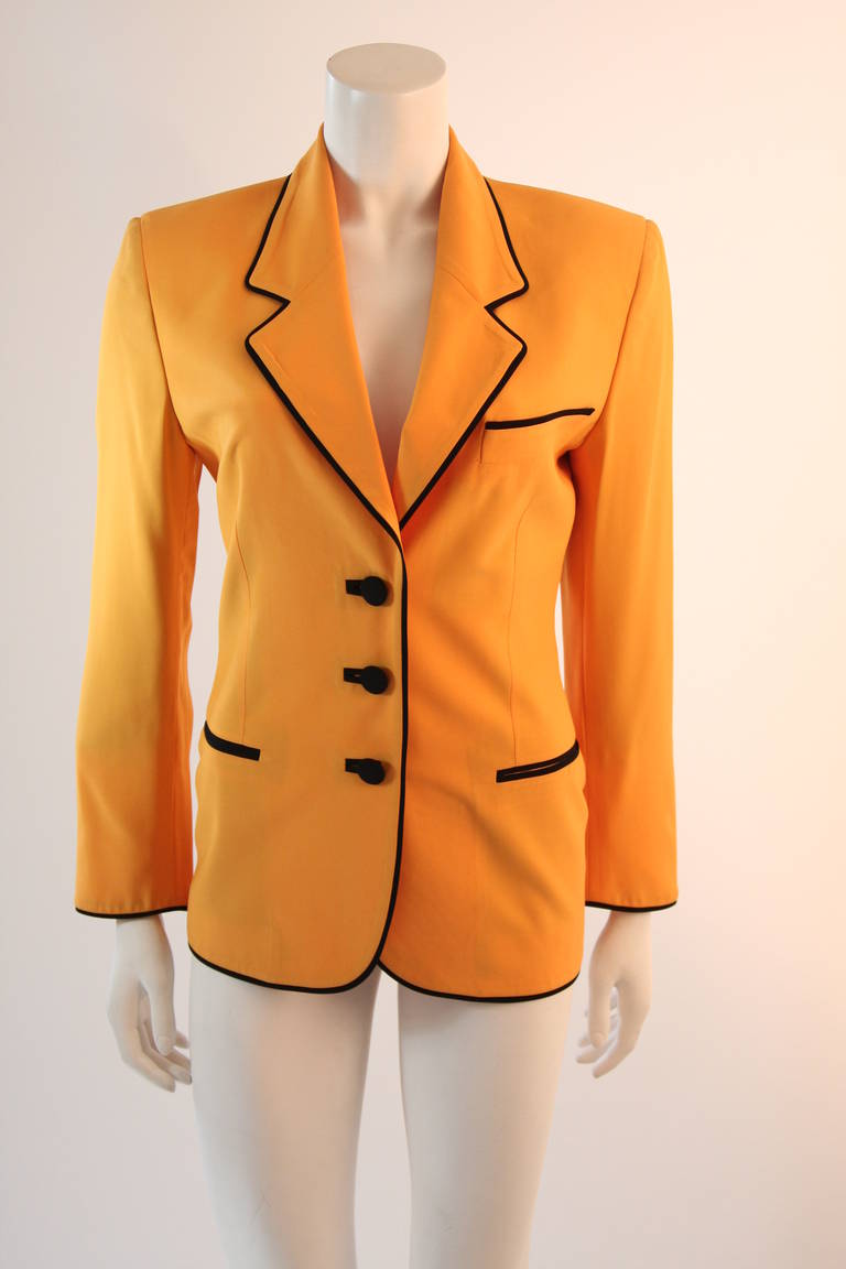 This is a brilliant Moschino design. This blazer is in an ultra hue of yellow and features black piping and trim through out the entire jacket. The jacket has two front pockets and center front buttons. The back displays a large 