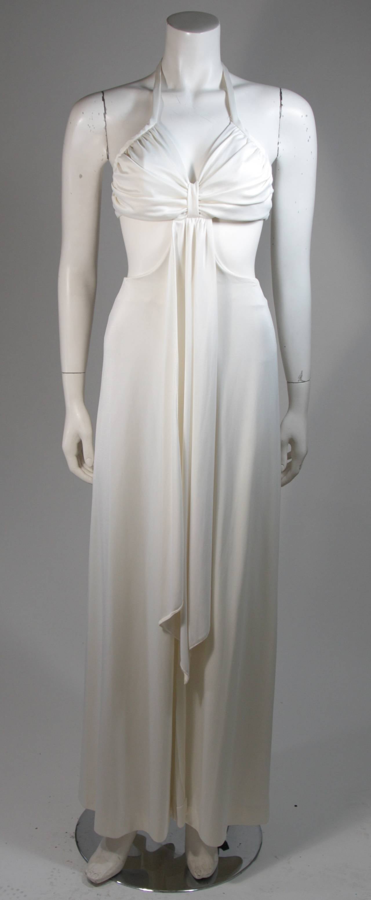 This Funky gown is composed of a white polyester jersey. The gown features a draped style with exposed sides and a center back zipper. In excellent vintage condition, there is one rust spot on the dress (see photos). 

**Please cross-reference