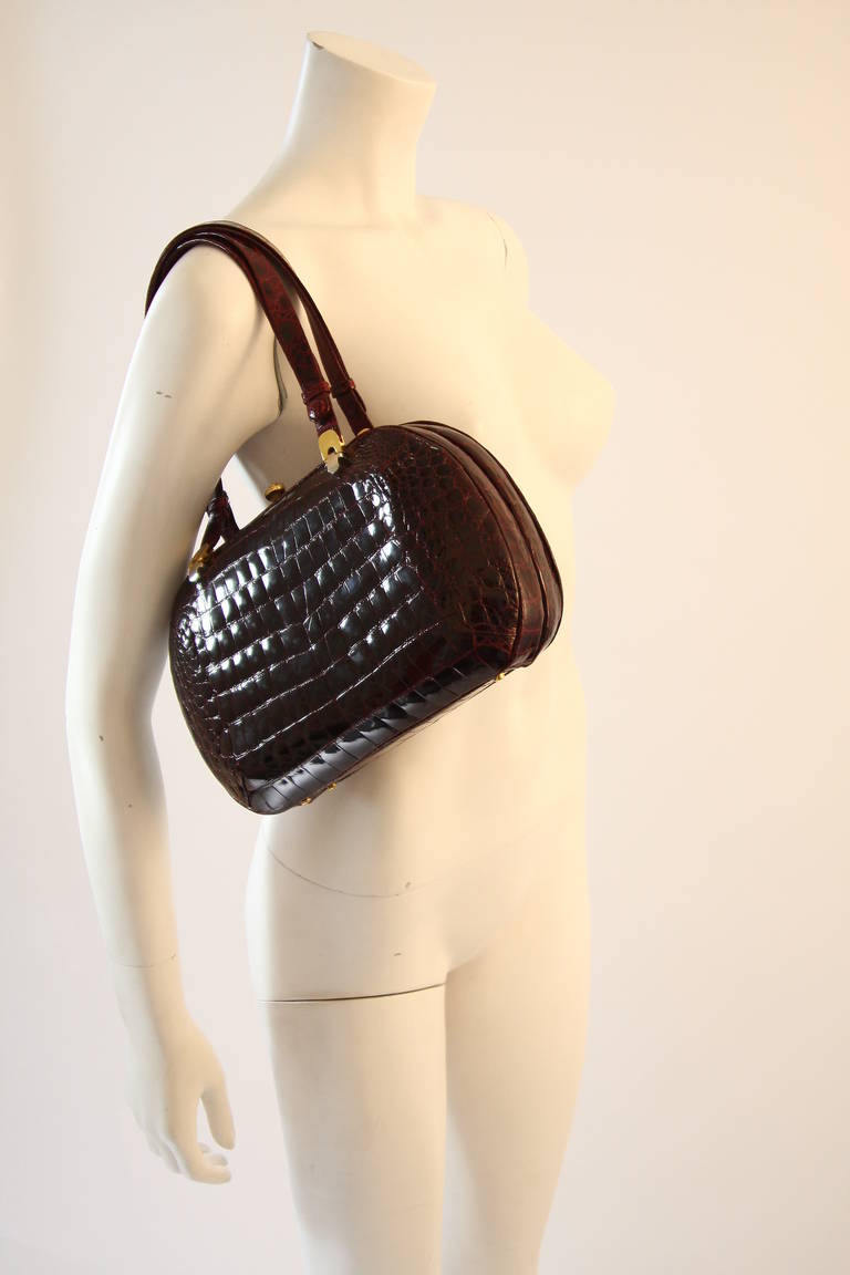 This is a stunning handbag by Nina Ricci. It is in a striking true shade of burgundy. The handbag is accompanied by a wonderful coin purse and mirror. The interior is in pristine condition and features three compartments (2 slide pockets and one