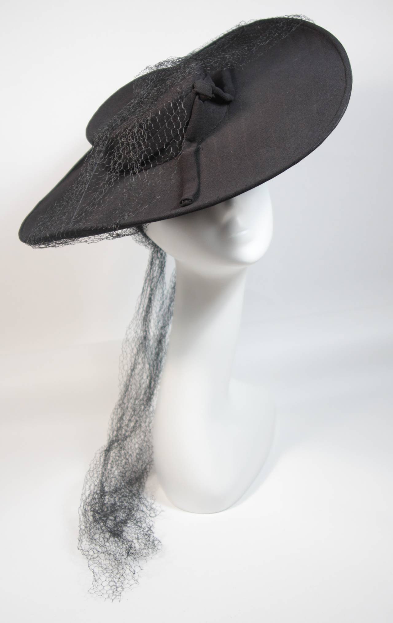 This Yvonne California hat is composed of a black material and features pin stripe stitch detailing. The hat is adorned with mesh and a bow. In excellent condition, the interior of the hat features some discoloration/fading (see photos). Made in