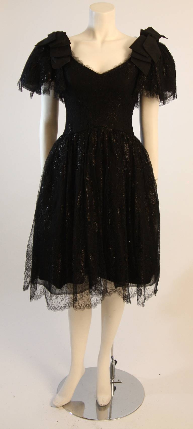 This is a lovely Nolan Miller cocktail dress. This dress is composed of a fantastic black supple lace with a subtle metallic attribute. It features a wonderful V-Bust line and draped sleeves with bow accents. The dress has boning for structure and a