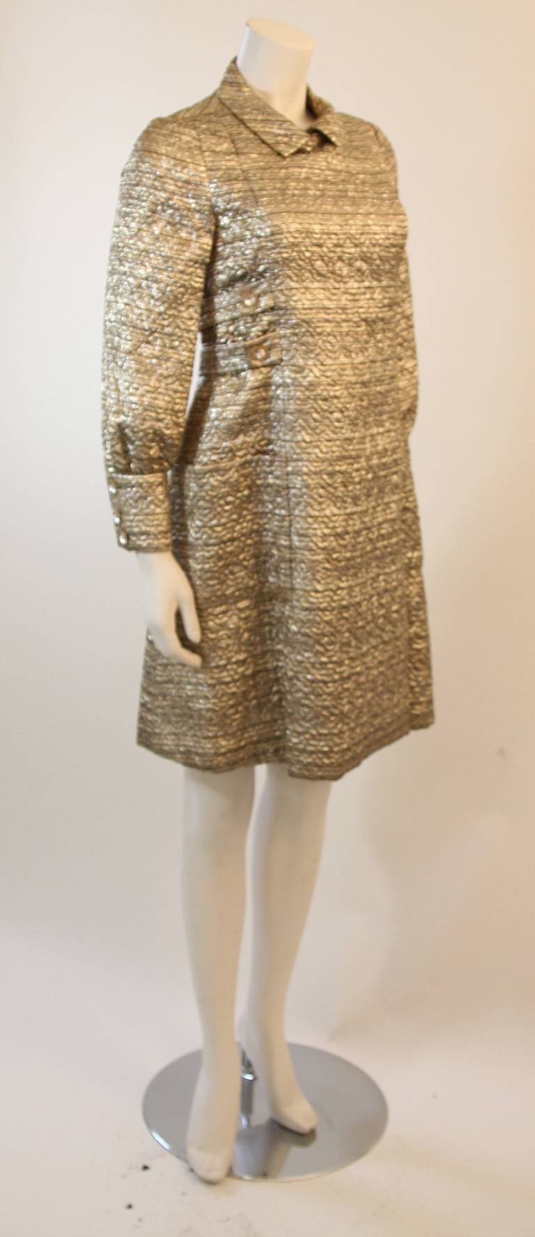 This is a chic Malcolm Starr design. This fantastic shift dress is composed of a wonderful metallic gold hued fabric accented with rhinestone buttons. The dress features button and snap closures. 

Measures (Approximately)
Length: 38