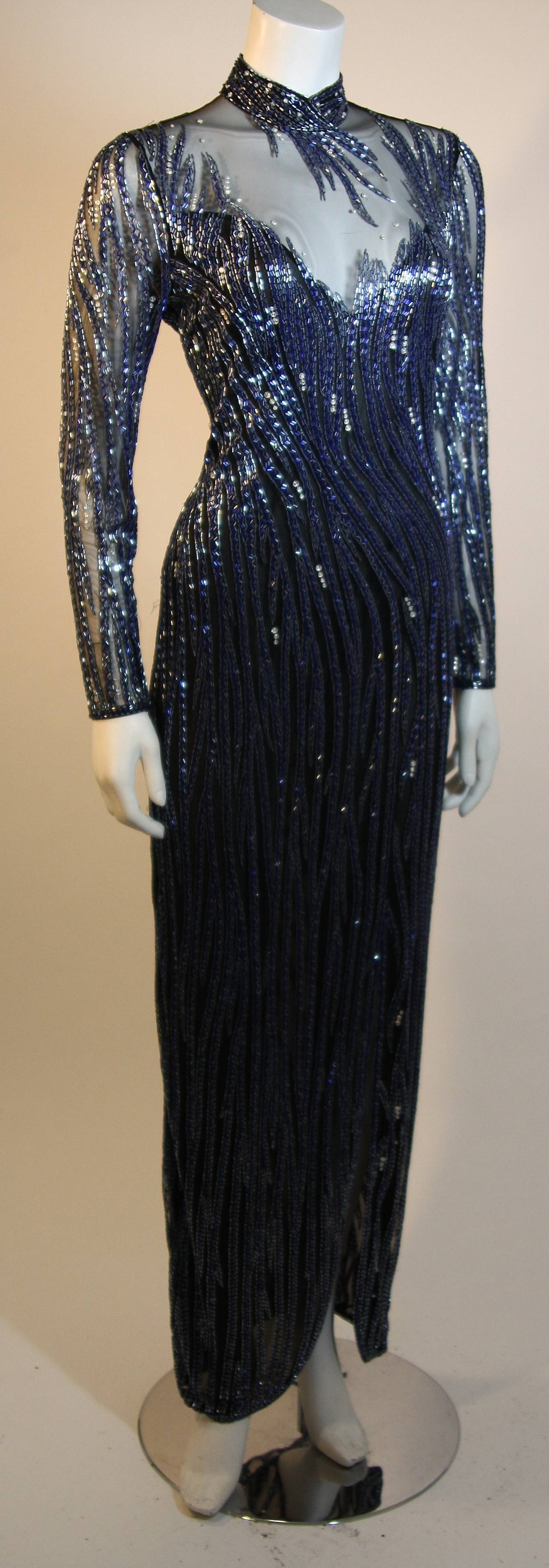 Beautiful glass beaded long sleeve gown adorned with varying shades of deep sapphire to blue silver over a sheer fitted black bodice, clinging hip, with an off-center slit at front. A smattering of rhinestones throughout add extra sparkle to this