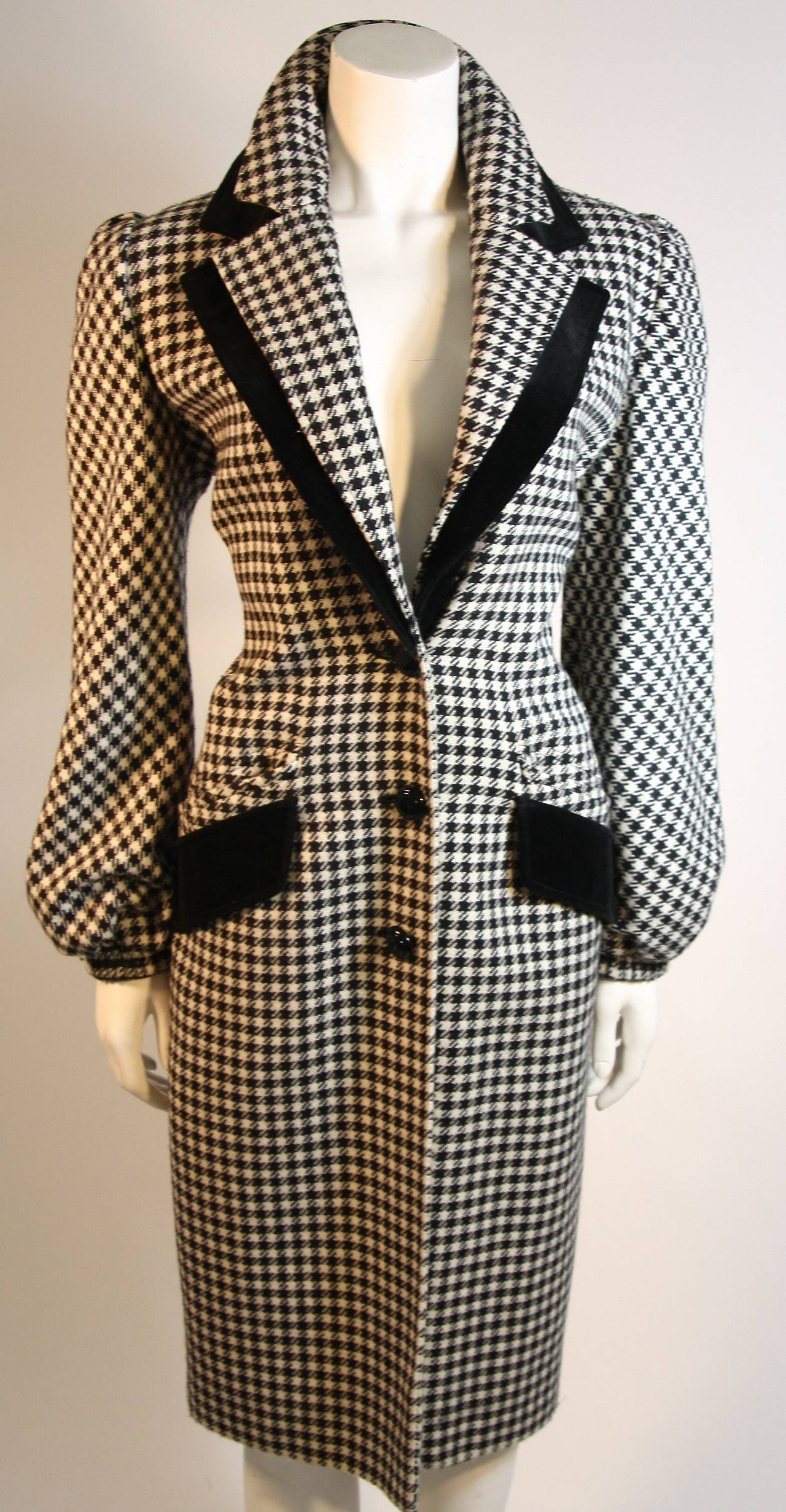 This is a Valentino coat. The coat is 3/4 length and features velvet accents. There is a double collar and two front pockets. The sleeves feature elastic cuffing and center front buttons. The fabric is a wool blend in a black and white Houndstooth