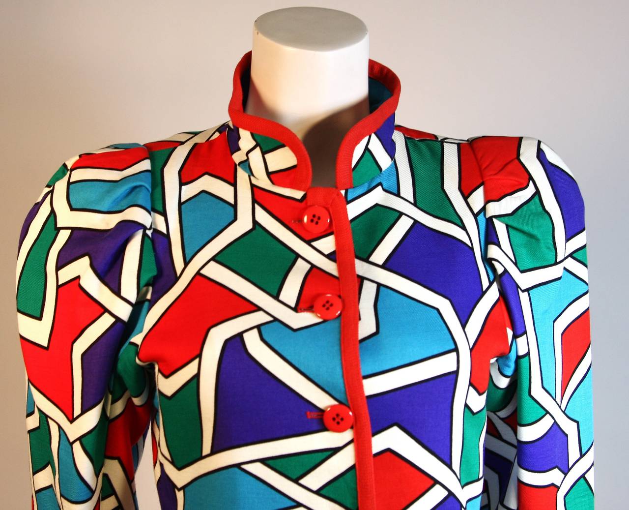 This is a Yves Saint Laurent design. This jacket features a wonderful color block print with mandarin collar and puff sleeve design. There are center front buttons for closure. The jacket is trimmed in red. Made in France. 

Measures