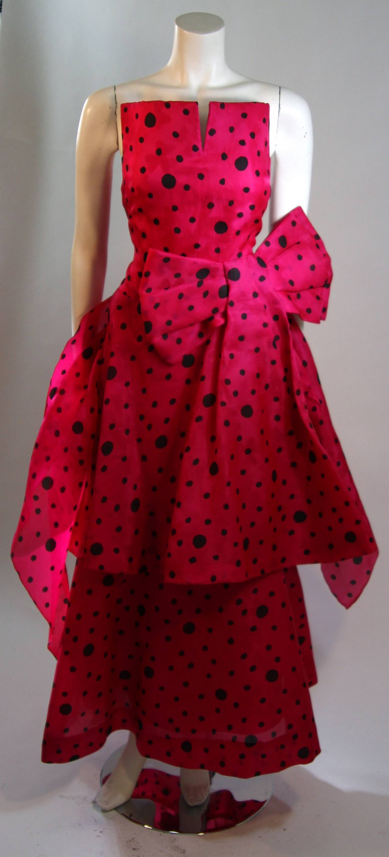 This is an Arnold Scaasi design. This wonderful gown is composed of a striking pink fabric with a black polka dot print. The gown features a structured neckline and an exaggerated bow plus layers fabric for a gorgeous silhouette. Comes with a shawl.
