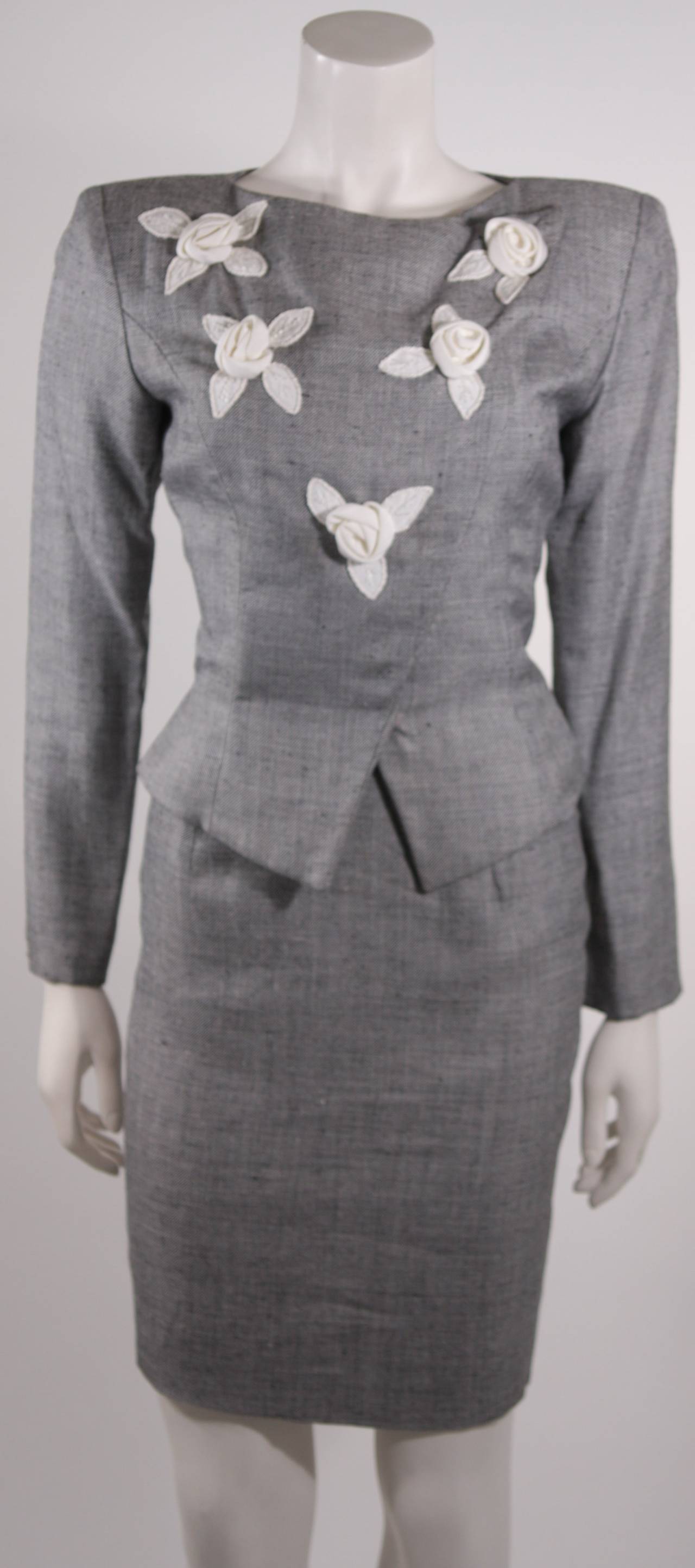 This is a phenomenal Vicky Tiel design. This skirt suit is composed of a fantastic wool and linen blend a fabulous shade of pale grey. The jacket is adorned in white flowers with an asymmetrical snap fastening. The skirt has a pencil silhouette with