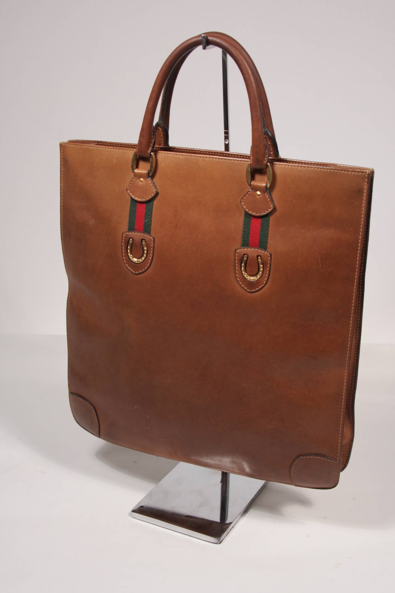 This is a Gucci vintage handbag. The tote style purse is composed of a wonderful cognac hued brown leather. It features a double strap design and is accented with gold toned horse shoes. The handbag is in good condition, yet shows signs of wear, the