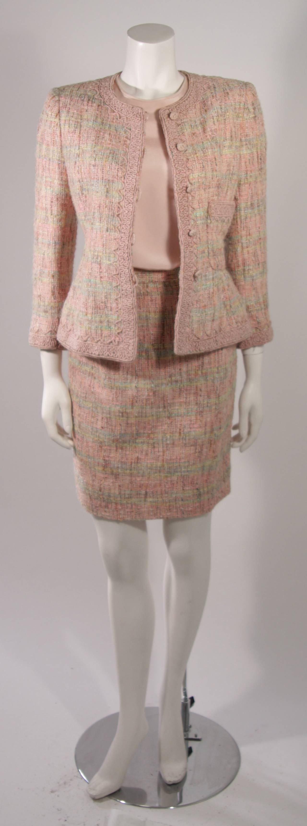 This is an Oscar De La Renta ensemble. The set features four pieces composed of a textured wool tweed accented with a pink embroidery trim, and silk. The jacket features center front buttons and two side front pockets. The skirt has a side zipper
