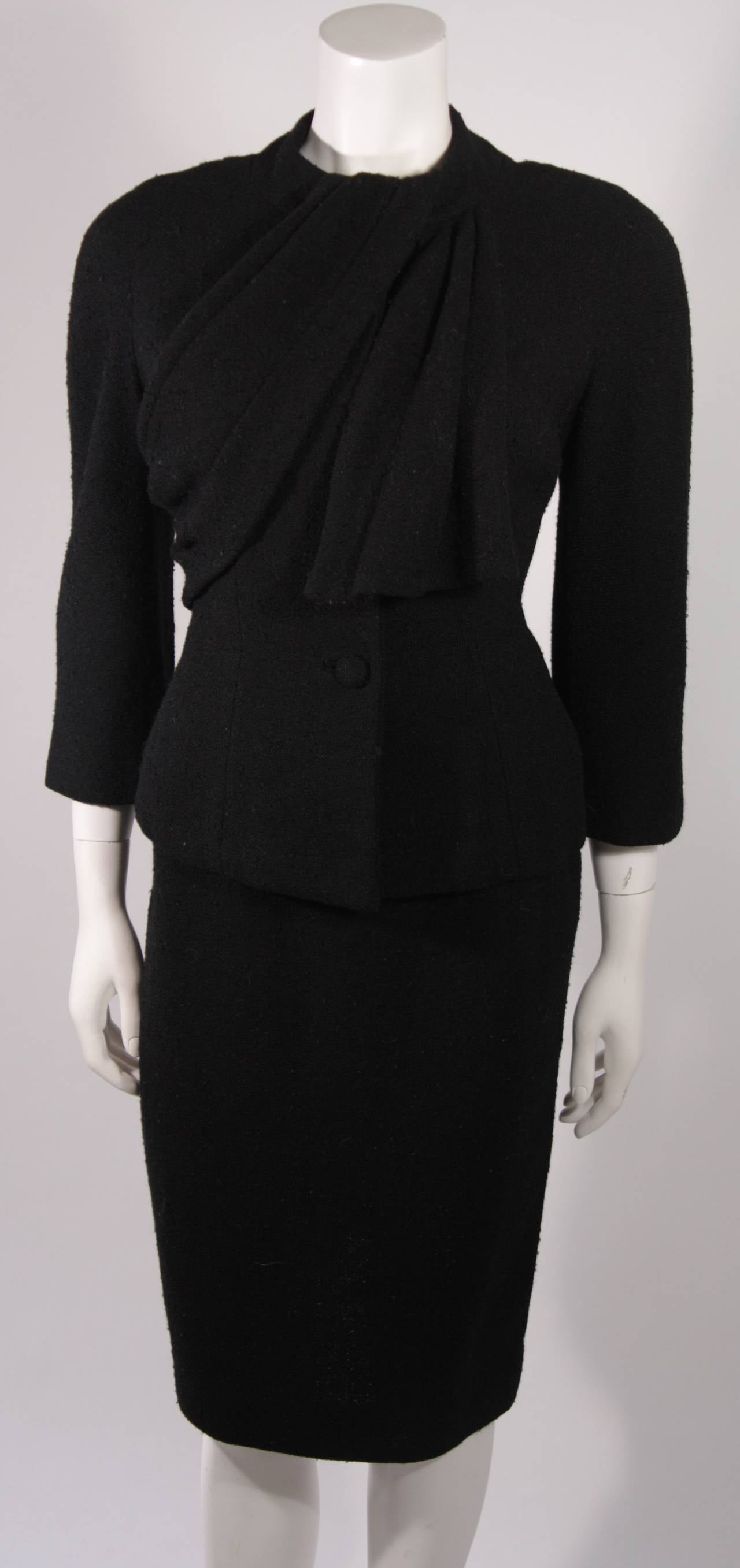 This is a Lilli Ann design. This stunning two piece suit is composed of fantastic black wool and features a brilliant draping from the neck. There are center front fastenings on the jacket and zipper closure for the skirt. 

Measures