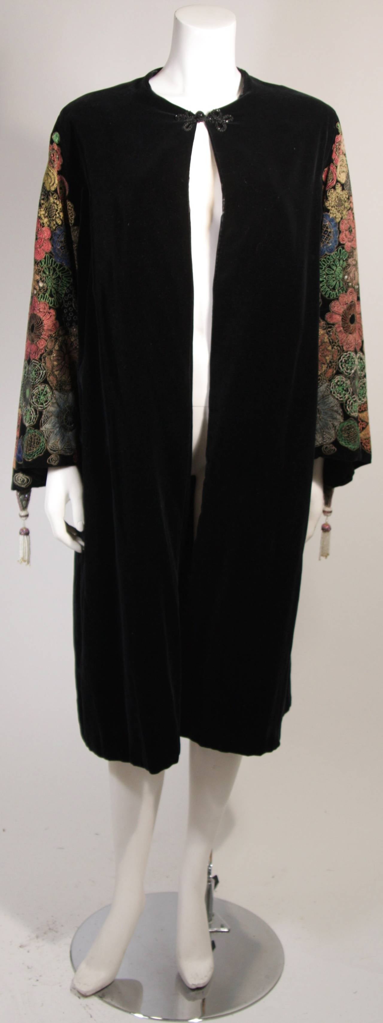 This is a black velvet coat. The coat features hand painted bell style sleeves adorned with a tassel. Features a beaded toggle neck closure. Velvet lined with silk. Circa 1930's.

Measures (Approximately)
Length: 44