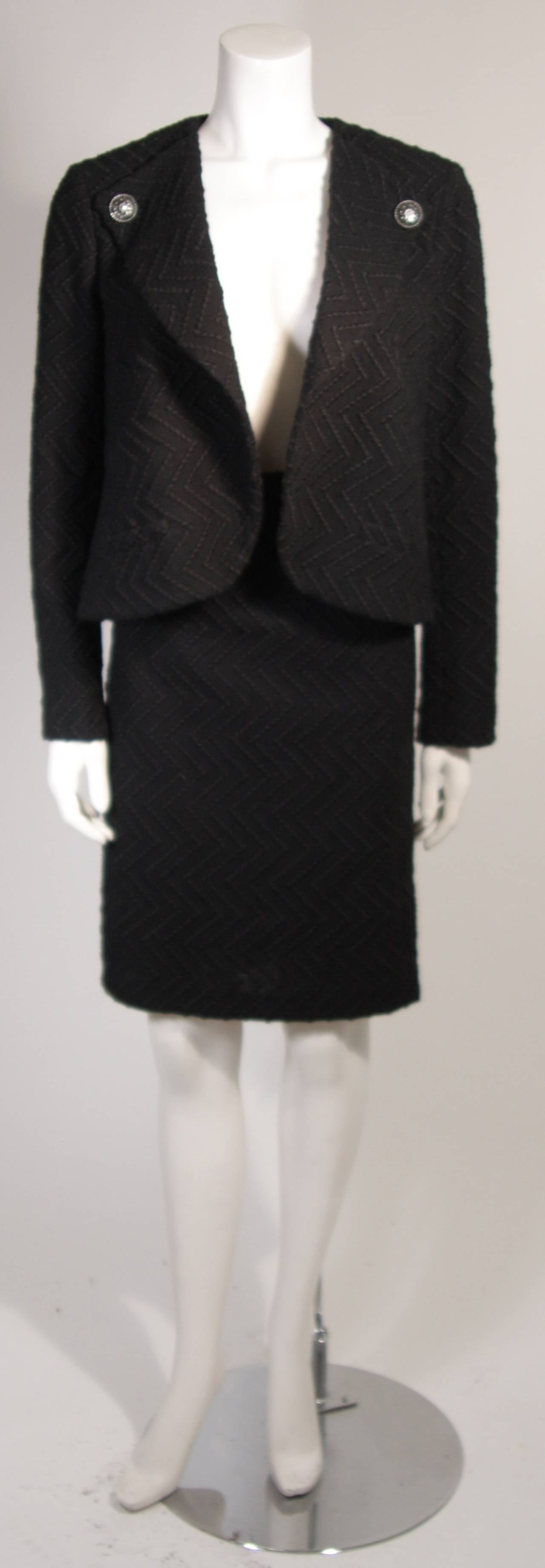 This is a Chanel suit. This suit features a drape style jacket and classic pencil skirt. The suit is composed of a supple black wool and has a lightweight silk lining with Chanel watermark logos. The jacket with drape style does not have any front