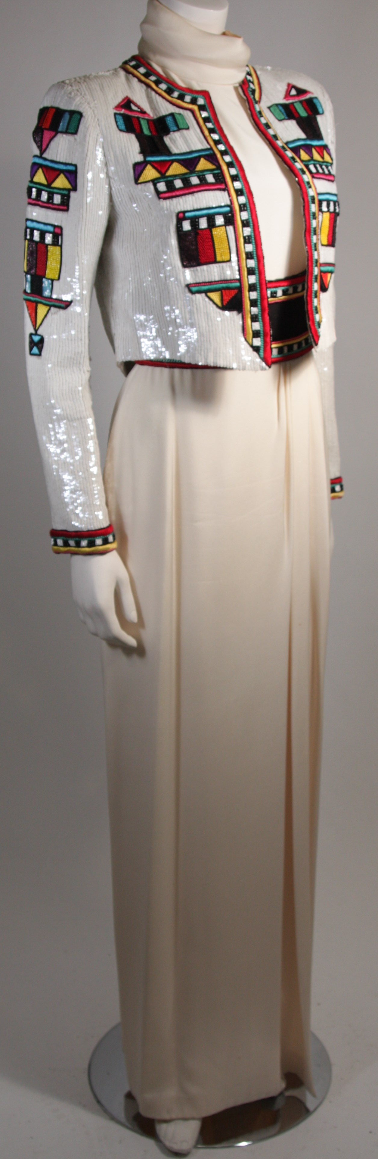 This is a Bob Mackie design. This ensemble features bold colored beading a top a warm Ivory neutral hue. The fully sequined evening jacket is heavily beaded with an ethnic pattern. The futurism style dress features a striking beaded waist detail and