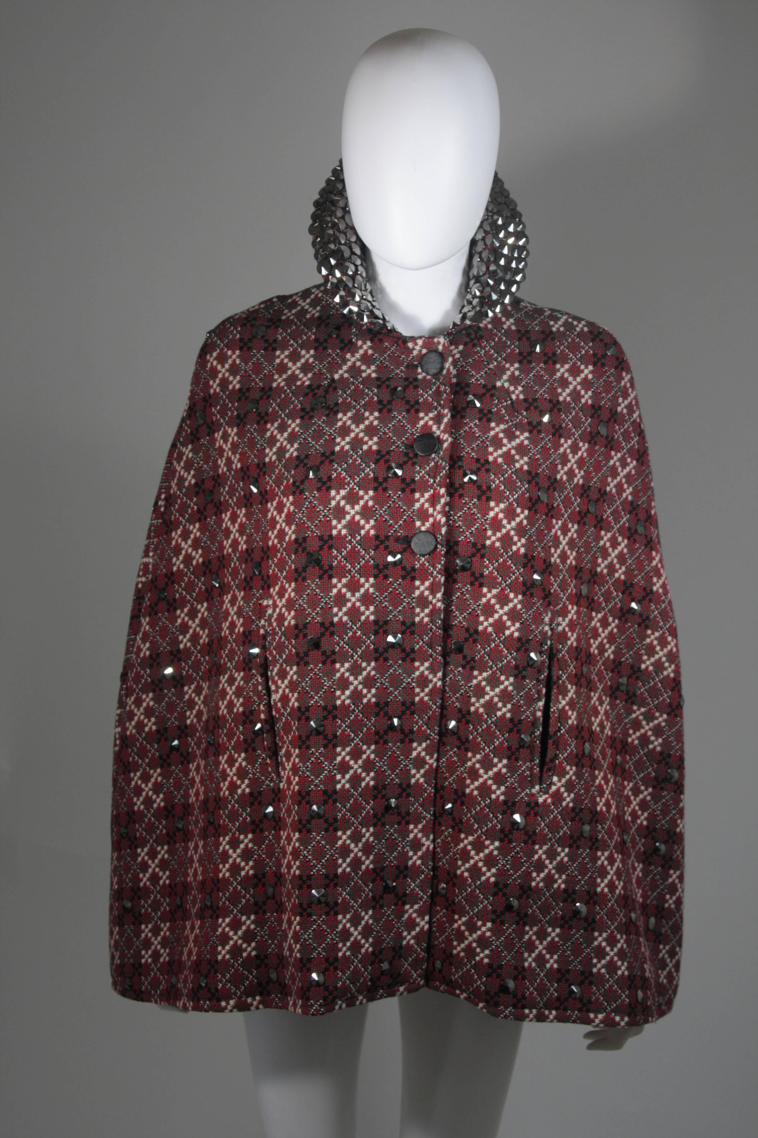  This cape is composed of a plaid wool, in red, green, and cream. The cape is a vintage design with a modern twist, the gunmetal hue embellishments are a modern addition by 'Vutique'. The jacket has a front button closure. In excellent vintage