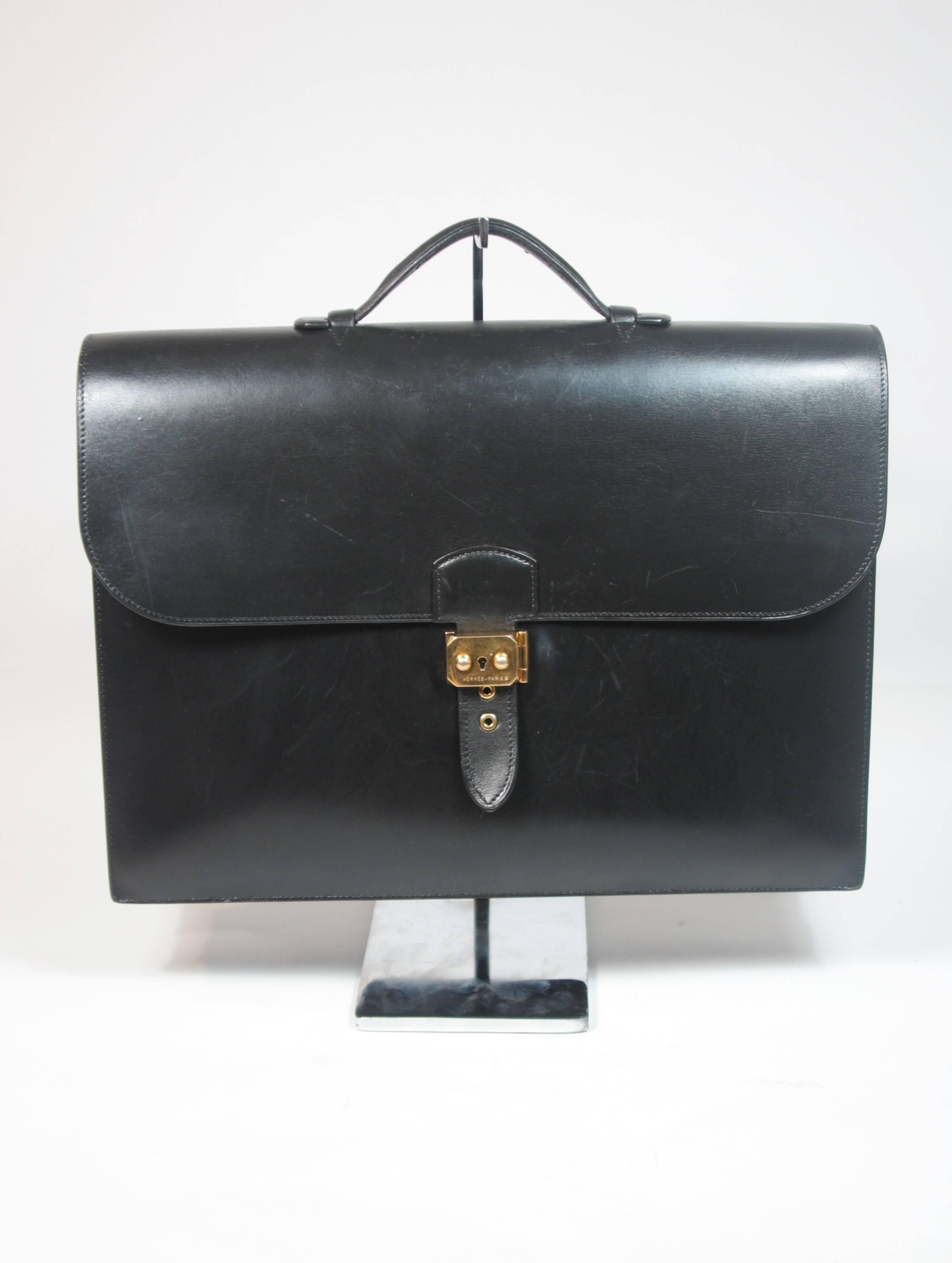 This Hermes briefcase is composed of a black box leather and features gold hardware. There is a top handle and three large interior compartments. The bag is in great vintage condition, there are some indentations at the top of the bag by the handle