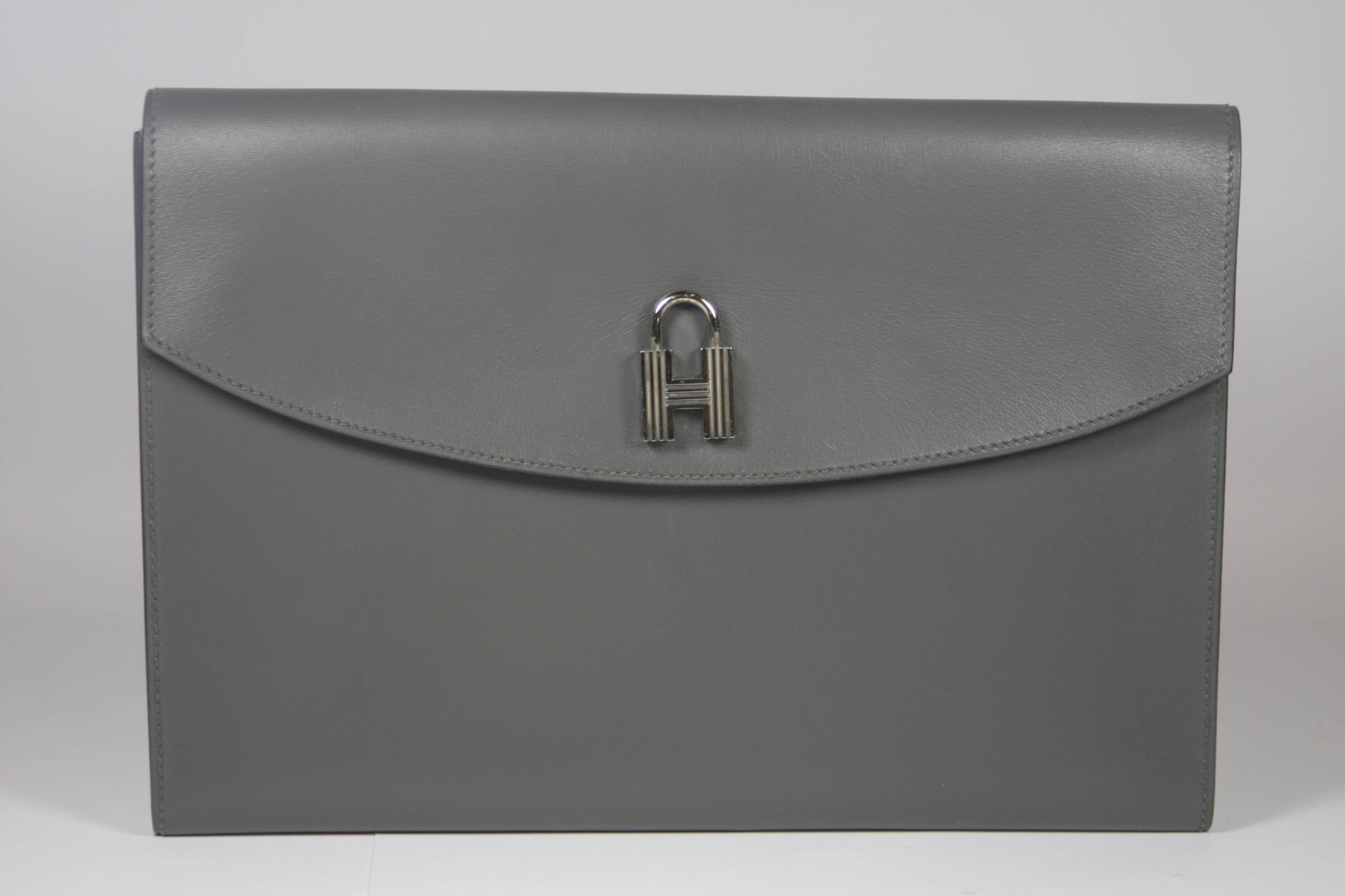 This Hermes clutch is composed of a stunning grey leather and features silver hardware. There is a silver mini non-functioning padlock detail on the exterior. In excellent rarely used vintage condition with Hermes sleeper bag.  Made in France.

 