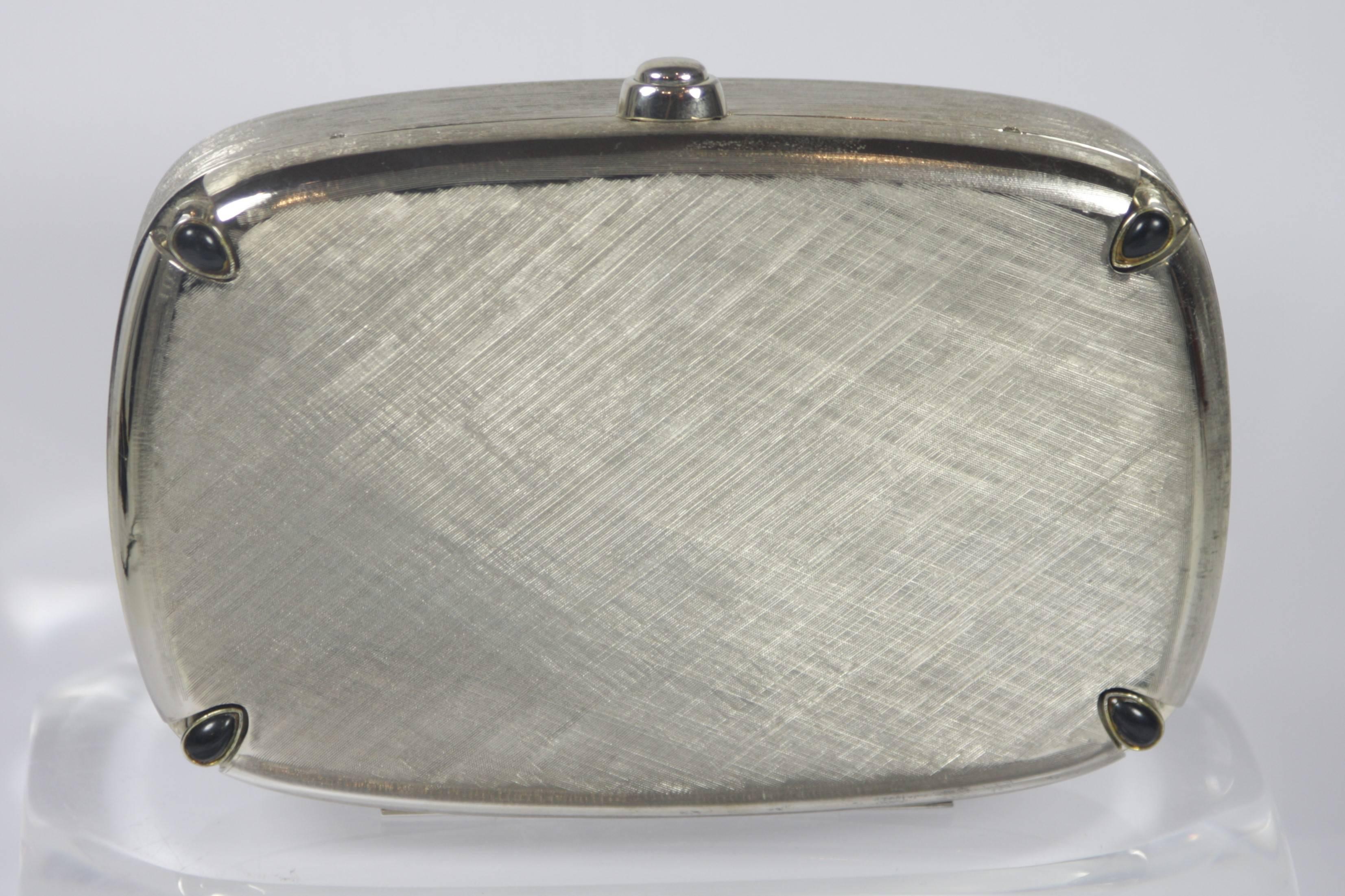 This Judith Leiber evening purse is composed of a silver tone metal with brushed detailing and stone accents at the corners. In excellent condition, comes with original comb, mirror, dust bag, and coin purse. 

**Please cross-reference