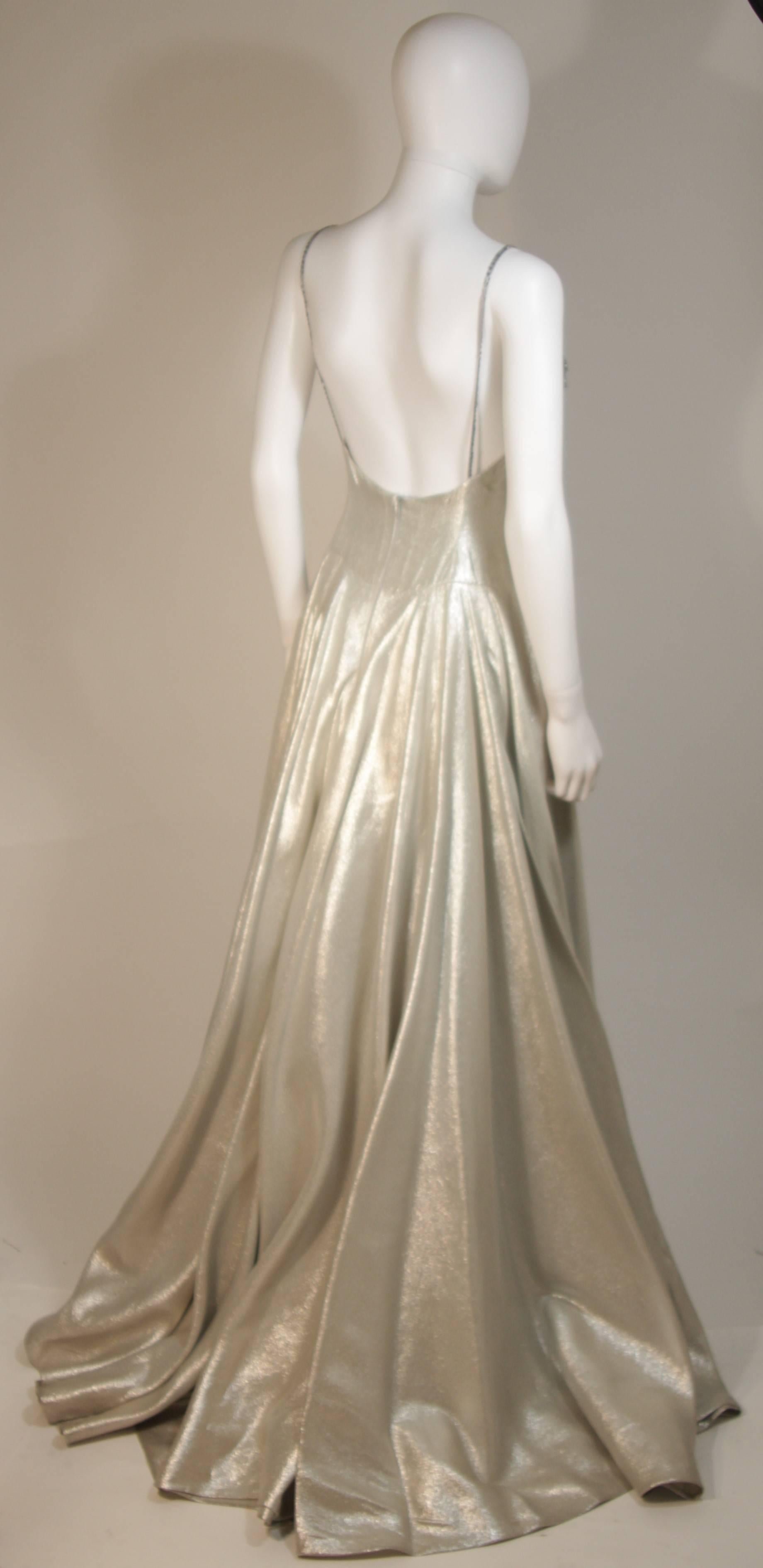 Dieses Ballkleid von Helen Rose besteht aus silberfarbener Metallseide und ist mit einem perlenbesetzten Oberteil versehen. Mit weit ausladendem Rock. Es hat Spaghetti-Träger und einen offenen Rücken. Es gibt einen Reißverschluss in der Mitte des