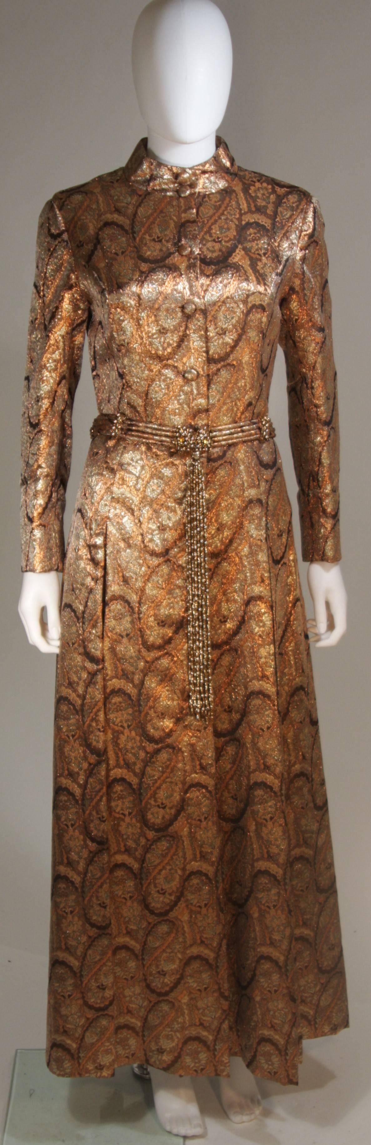  This Dynasty  coat is composed of a bronze paisley fabric with a beaded belt. The jacket has a mandarin collar, side pockets, and flare skirt. There are center front closures. In excellent vintage condition, there is fraying at the shoulders, which