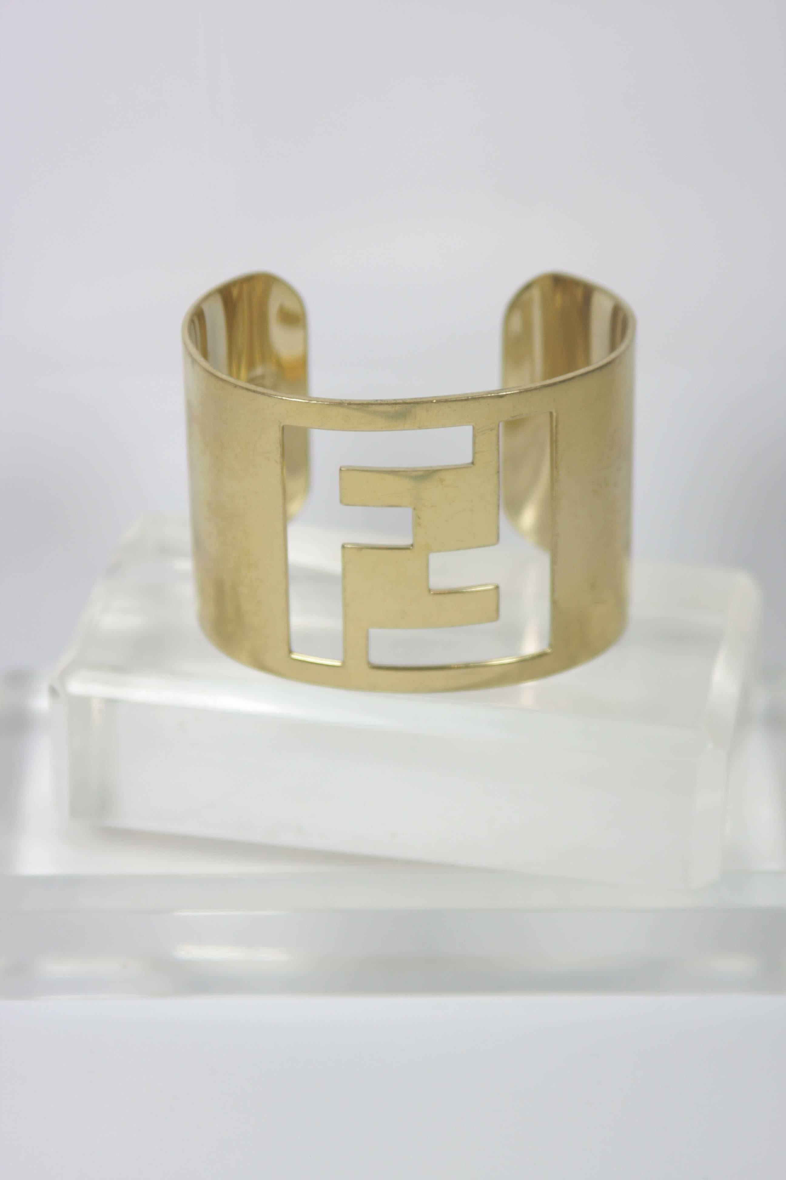  This Fendi design is available for viewing at our Beverly Hills Boutique. We offer a large selection of evening gowns and luxury garments. 

 This cuff style bracelet is composed of a gold tone metal and features the classic Fendi logo. In good