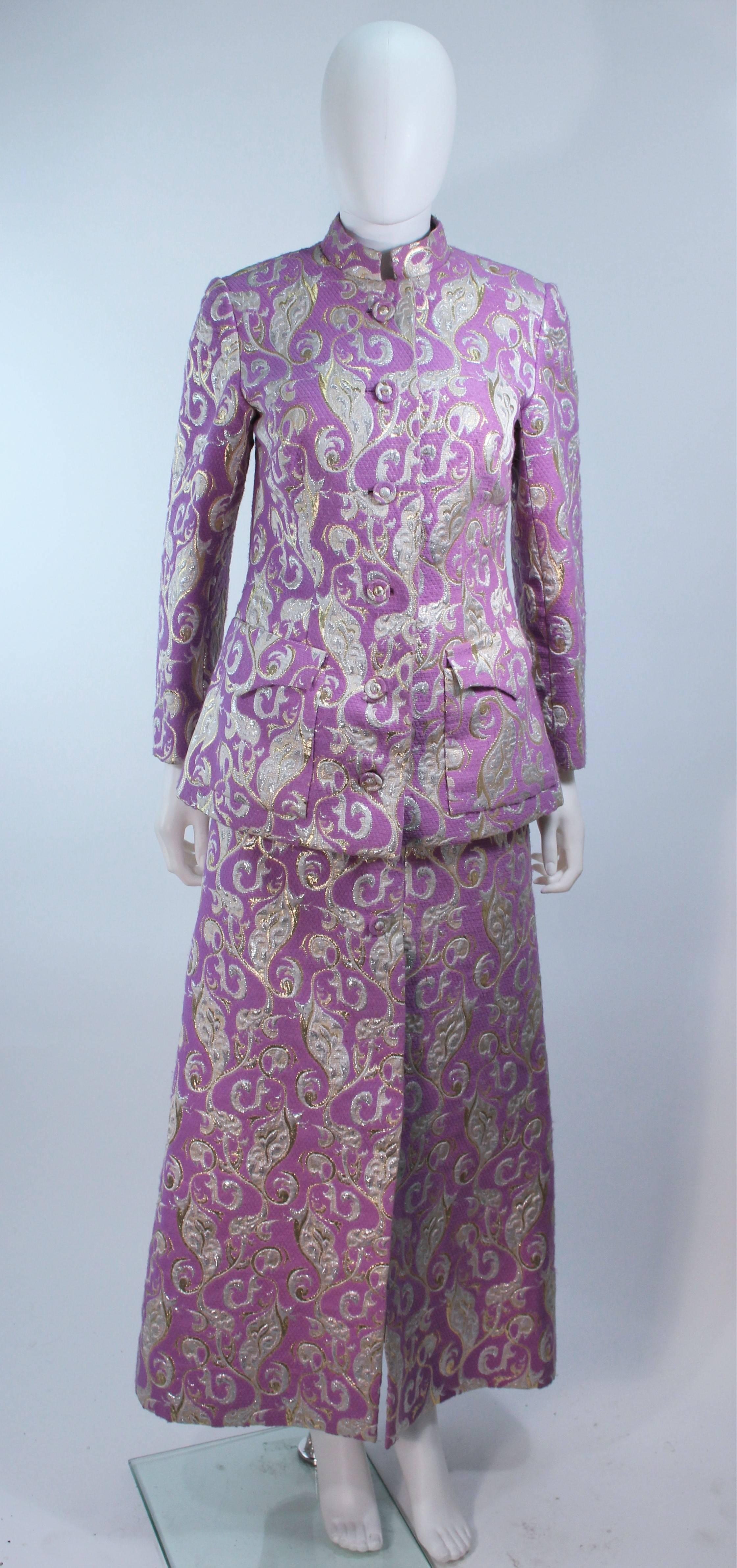  This ensemble is composed of a purple (lilac/lavender) hue brocade with metallic accents. The jacket and skirt feature center button closures. The Jacket has a mandarin/safari style. The skirt has button accents and a zipper closure. In great