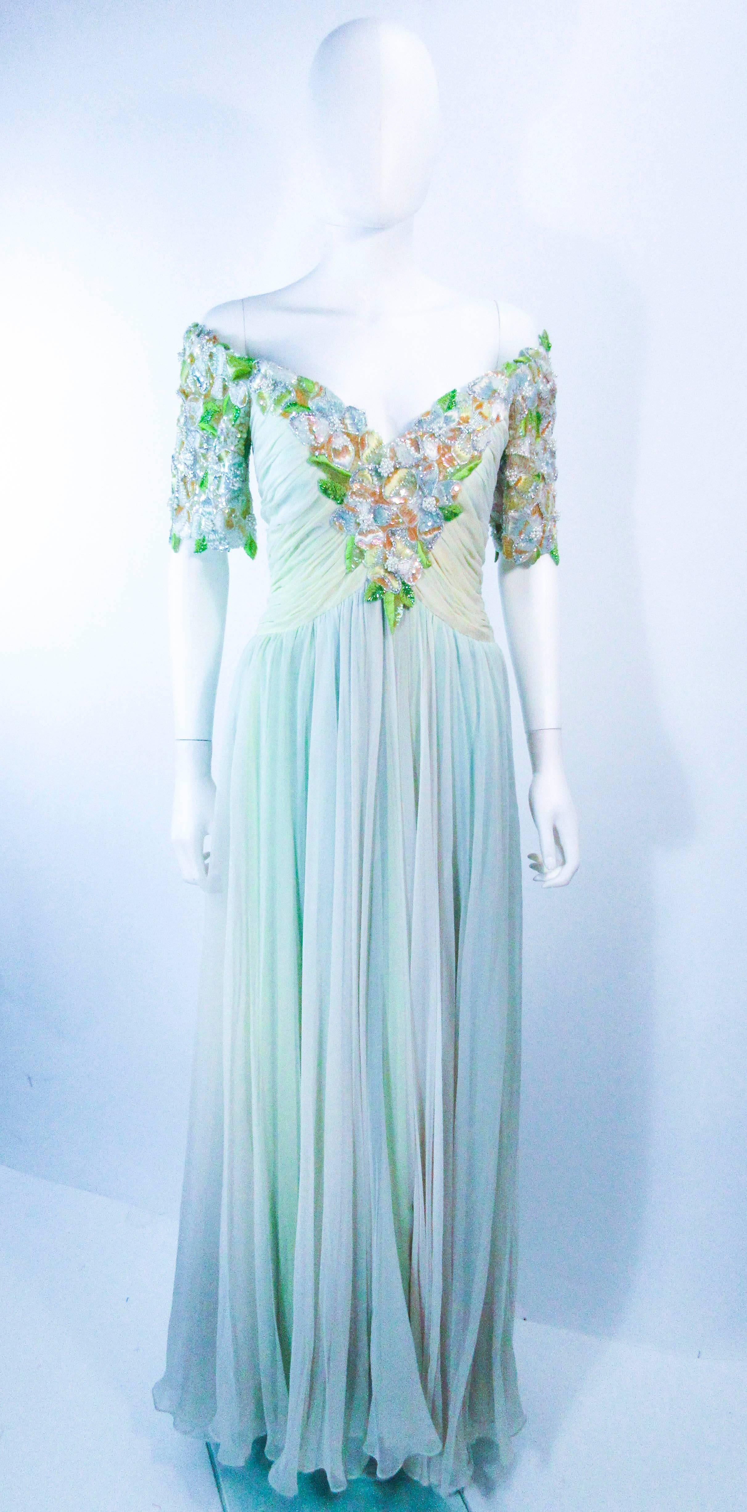 This vintage Bob Mackie gown is composed of a light green mint hue silk chiffon. The upper bodice features an embellished center front and short sleeve, with a floral pattern. There is a zipper closure with structured interior. In 