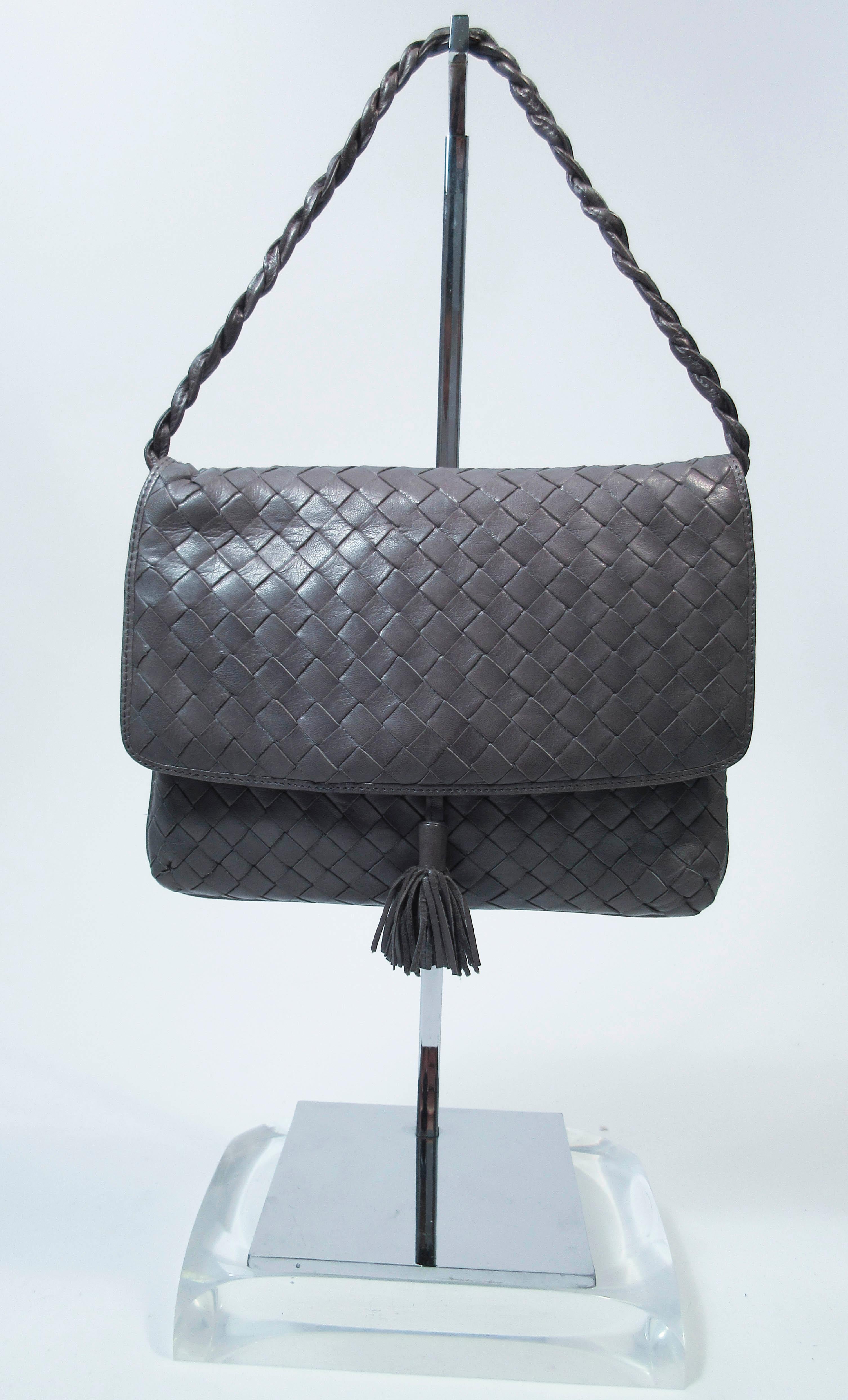 This vintage Bottega Veneta purse is composed of a grey supple leather. Made in Italy. Features a single woven drop strap. There is one interior zipper pocket & one slide pocket. In excellent pre-owned condition (some signs of wear due to age, see