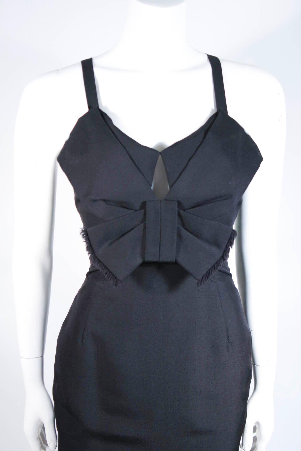 Fashioned from the finest black Silk Dupioni, this exquisite cocktail dress features a gorgeous body skimming silhouette. There is a peek-a-boo accent and large bow detail at the bust with a raw edge. Such a fabulous and chic design.

This is a