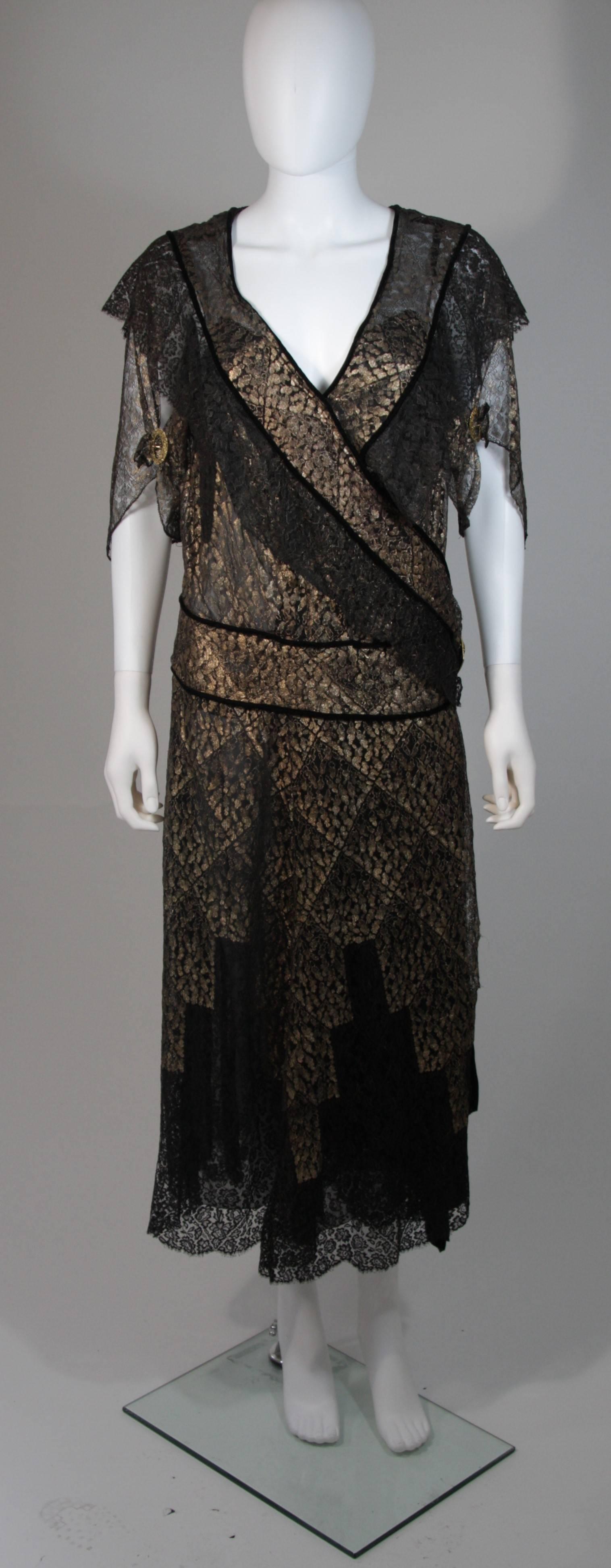 This vintage 1920s dress is composed of a black and gold lace which features a velvet trim. The wrap style dress features hook and eye closures, and snap closures. The waist and sleeves are adorned with different variations of gold/bronze hued
