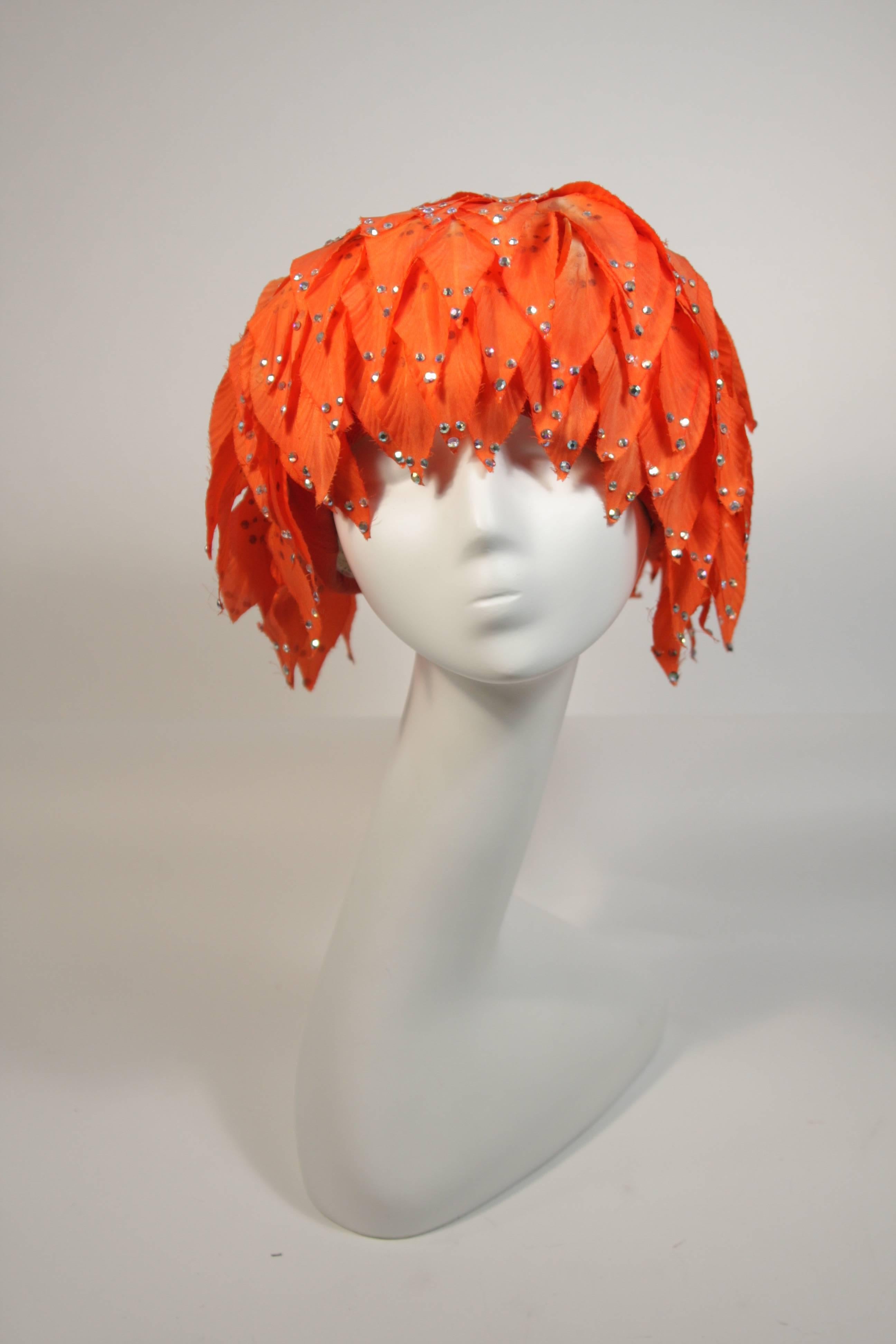 This Jack McConnell hat is composed of orange petals a-top a mesh base. The petals are adorned with rhinestones. The hat is in good condition for design inspiration and as a collectors item, there are missing rhinestones and discoloration (see