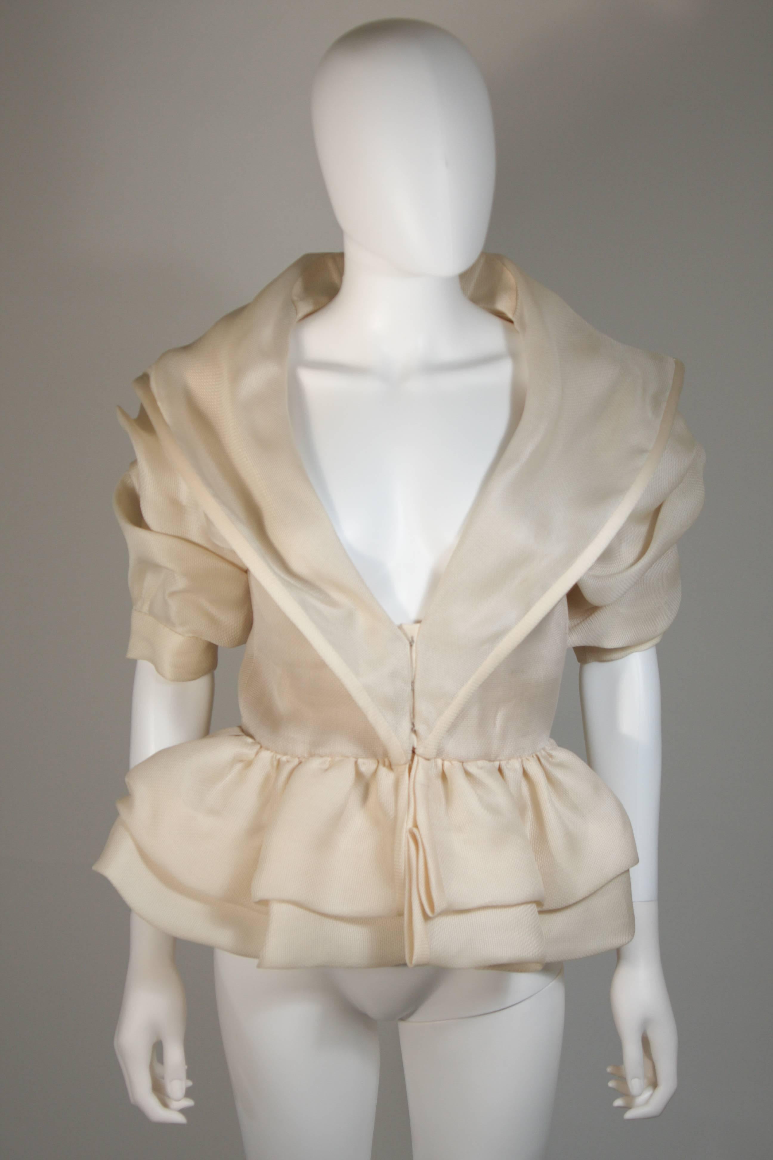 This Paul Louis Orrier Paris jacket is composed of an ivory/cream hued silk and acetate. The ruffled ivory fabric is accented by a structured hem. There are center front hook and eye closures. In excellent condition. Made in France.

**Please