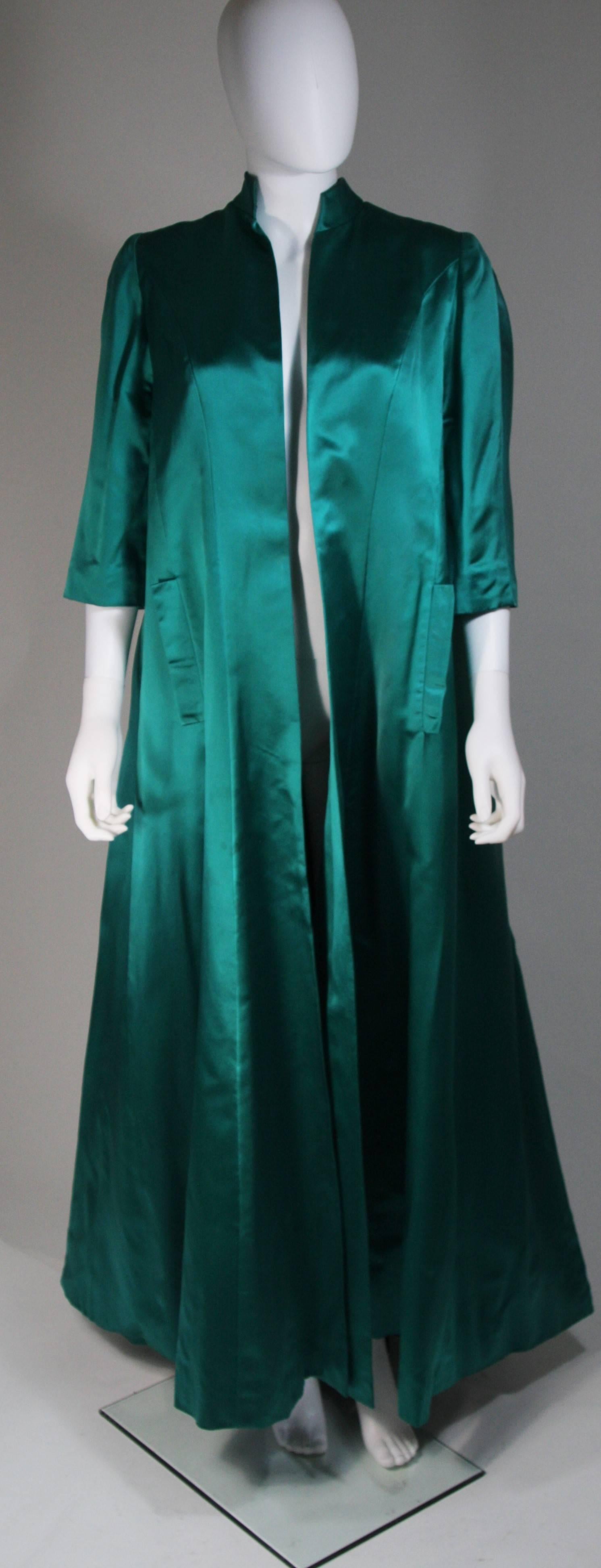 This Galanos coat is composed of a green silk, in an emerald teal hue. The coat has an opera style  featuring godets for flare. There are front pockets, and an open style without closures/fastenings. The coat shows some wear and discoloration, it is