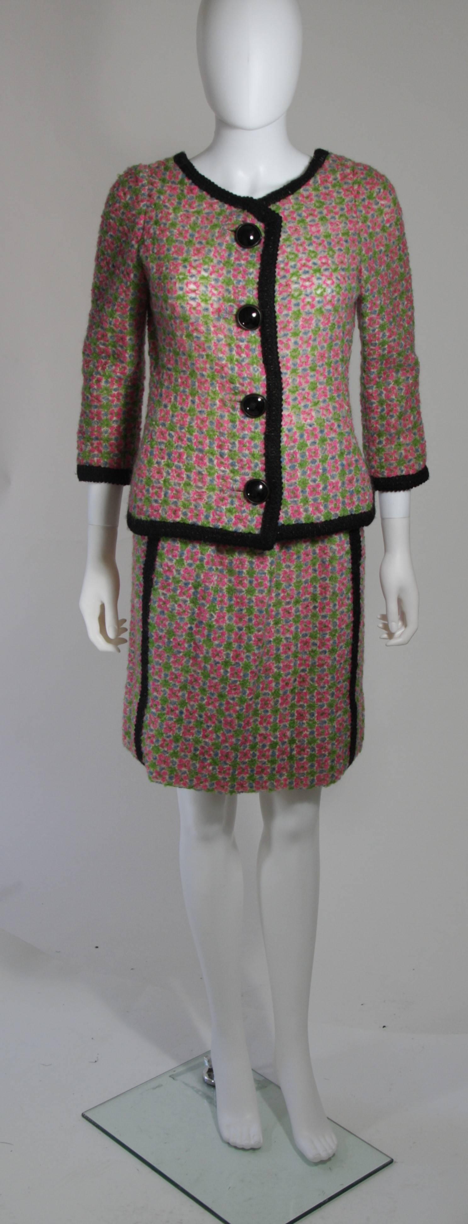 This Galanos skirt suit is composed of a knit wool fabric in green, pink, white, black color combination. The jacket features center front buttons. The set is accented with a black trim. The skirt features a side zipper and one side pocket. In