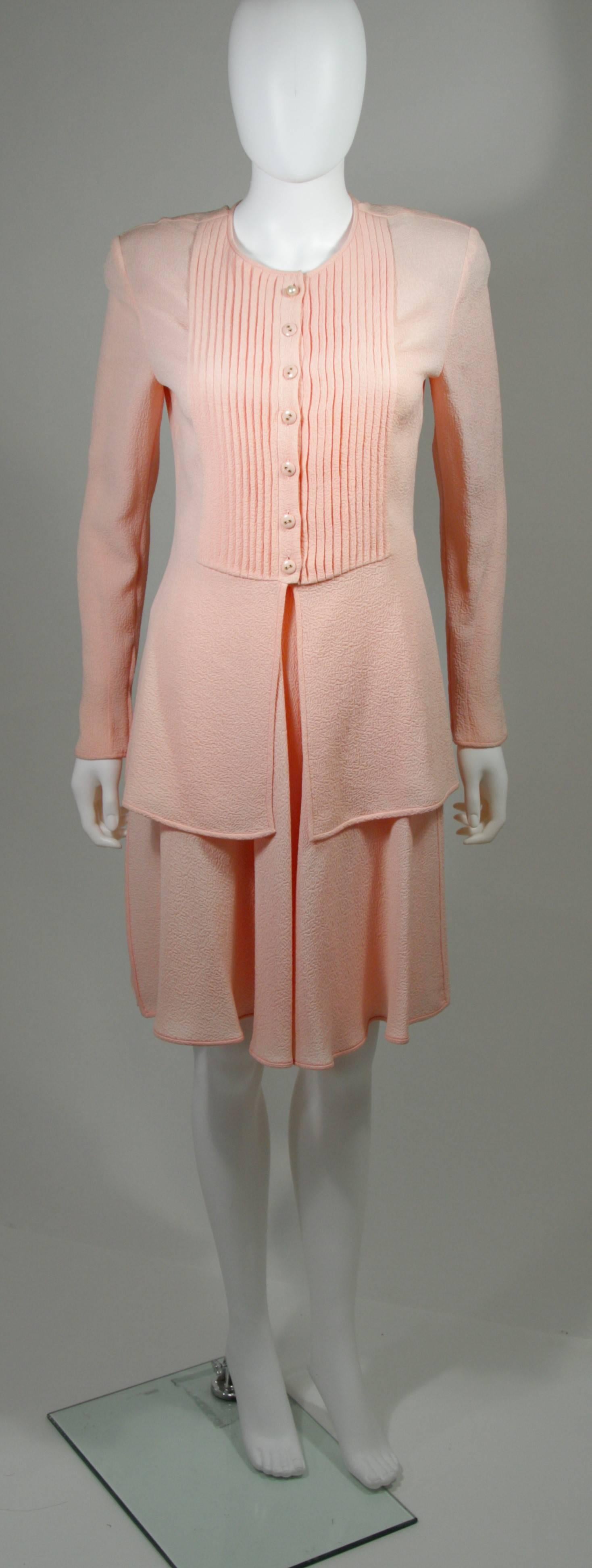 This Valentino skirt set is composed of a pink silk. The blouse features a pleated front with buttons and zippers at the sleeves. The skirt features a large pleat style with side zipper closure. There are shoulder pads. In excellent condition. Made
