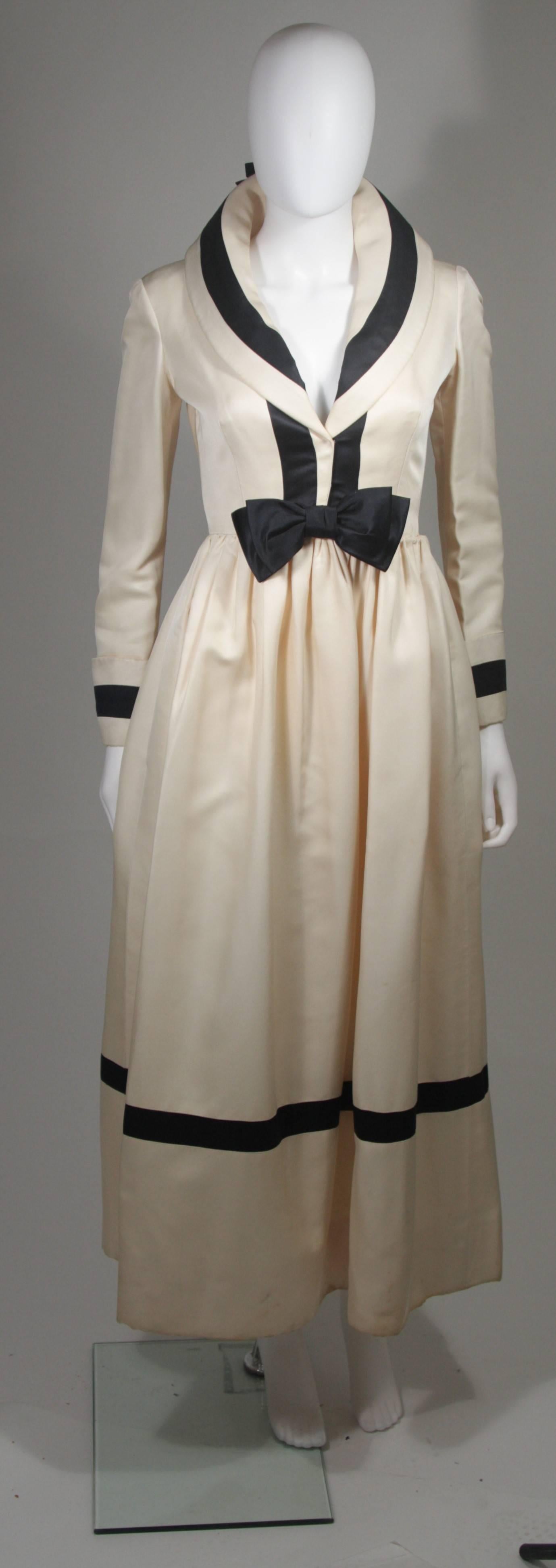 This Geoffrey Beene dress is composed of a cream silk and features black satin trim. There are center front closures, side pockets, and an attached belt detail. Sold in 