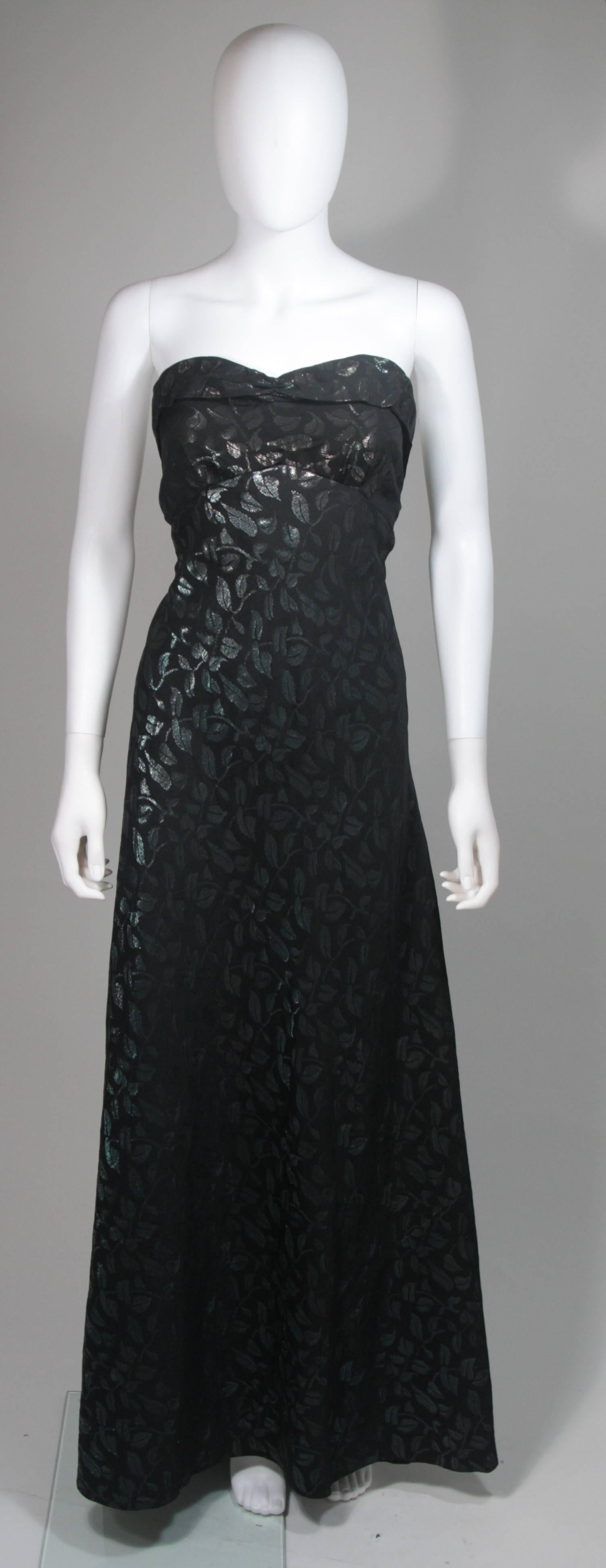 Cette robe vintage est composée d'une soie noire ornée d'un motif de feuilles dans des teintes métalliques bleues et vertes. La robe présente un corsage ajusté et une jupe évasée. Les boutons sont situés au centre du dos. Vintage, en excellent état.
