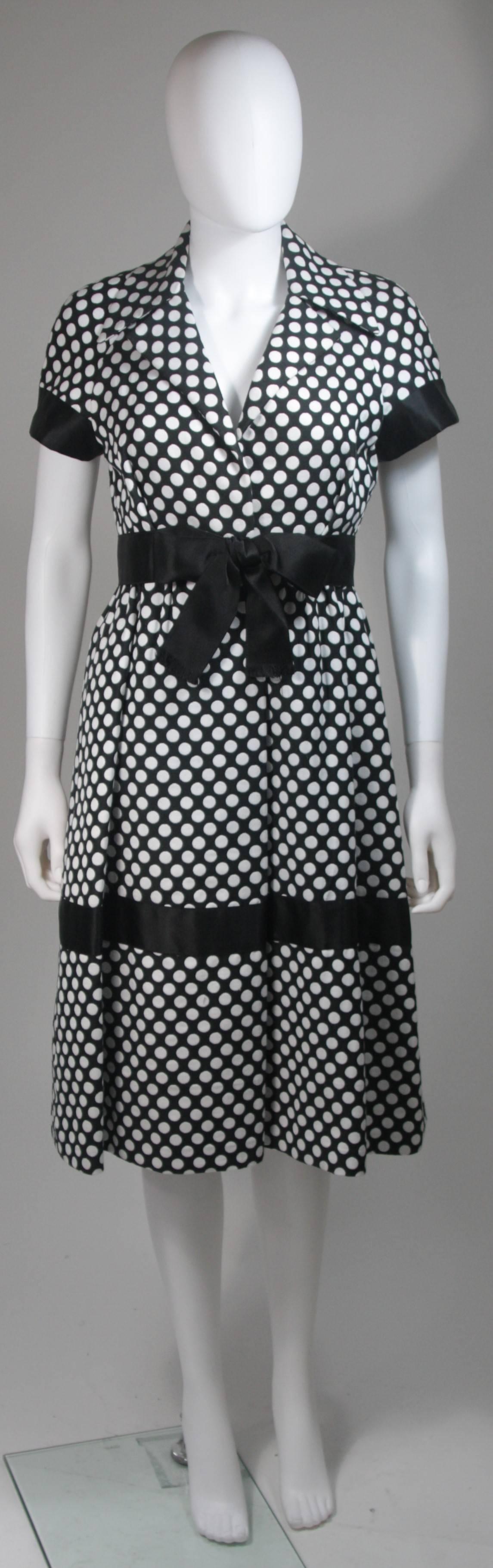 This Geoffrey Beene dress is composed of a black and white polka dot fabric. Features satin trimming and bow. There are center front hook and closures as well as snaps. The design has a large collar and pleat flared skirt with side pockets. In