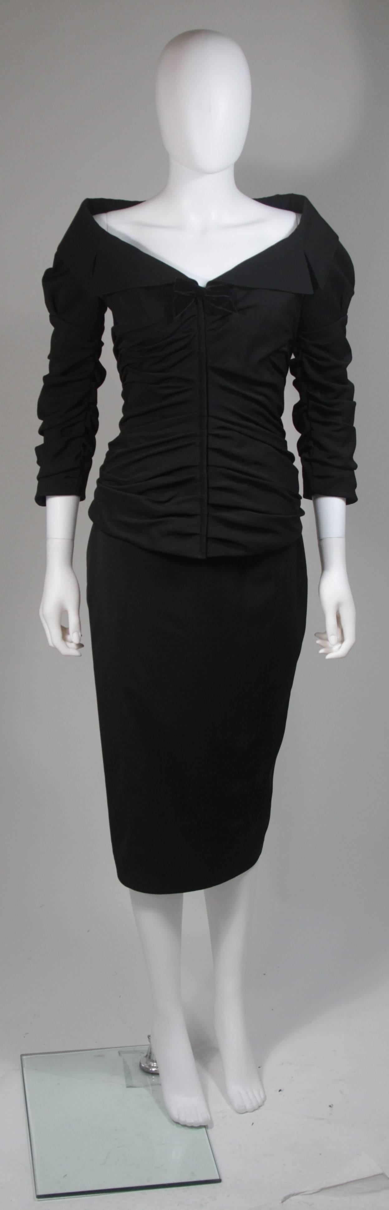This Thierry Mugler skirt suit is composed of a black material and features rouching throughout the jacket. The jacket has a center front zipper and velvet bow, along with an off the collar design. The skirt has a classic pencil silhouette with