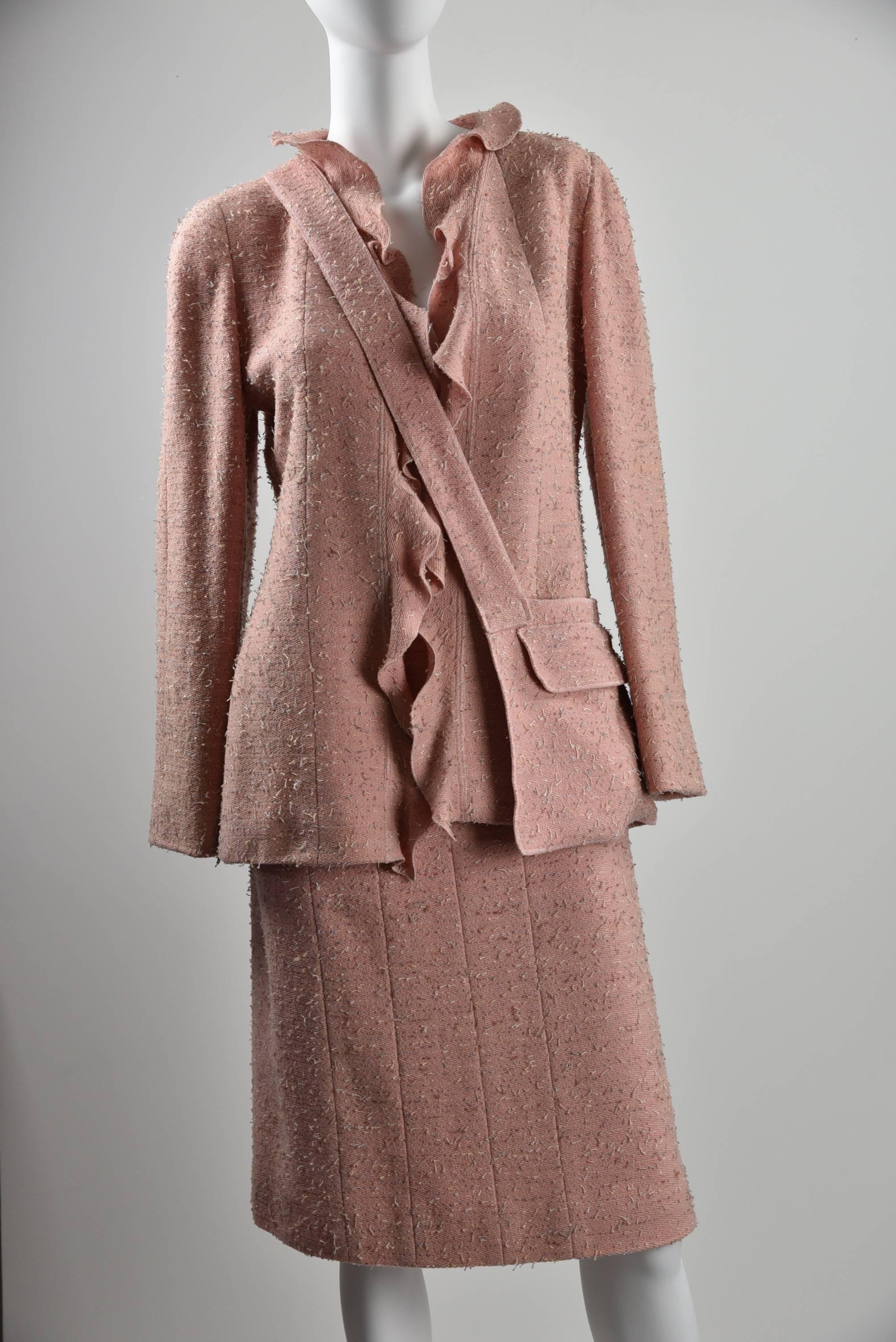 Suit is pink with tweed yarns of brown and ivory.83% wool, 15% polyester,2% nylon, lining is 95% silk and 5% spandex.  The matching pouch has a silver CHANEL identifier.  Chanel buttons are conspicuously missing from this garment, using the ruffled