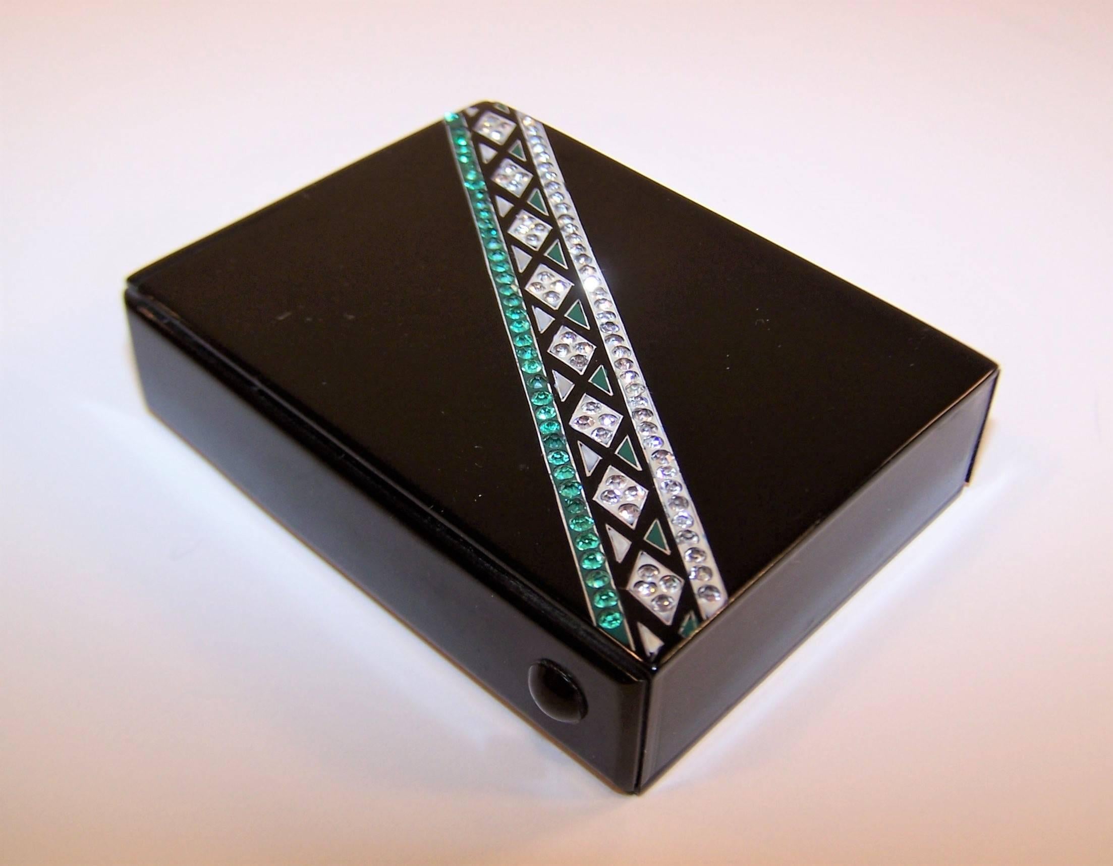 'Sleek and glamorous' are just some of the ways to describe this Art Deco cigarette case.  The black plastic box is decorated at the front with a classic Art Deco linear motif in silver and emerald green with coordinating pave crystal
