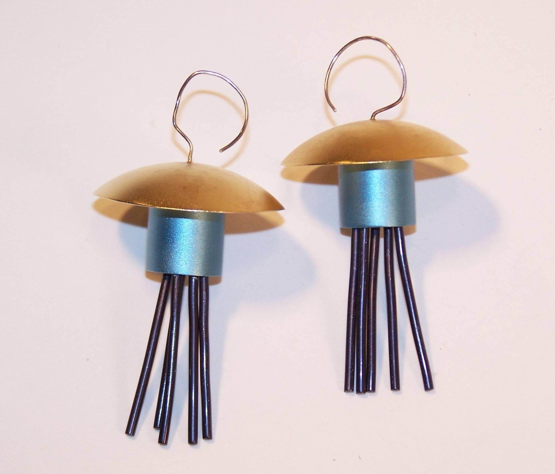 The wit and whimsy of the Memphis design movement is apparent in these charming earrings.  The anodized aluminum gold and frosty aqua blue bases suspend articulated black rods creating both movement and a sculptural style. Whether you see pagodas,