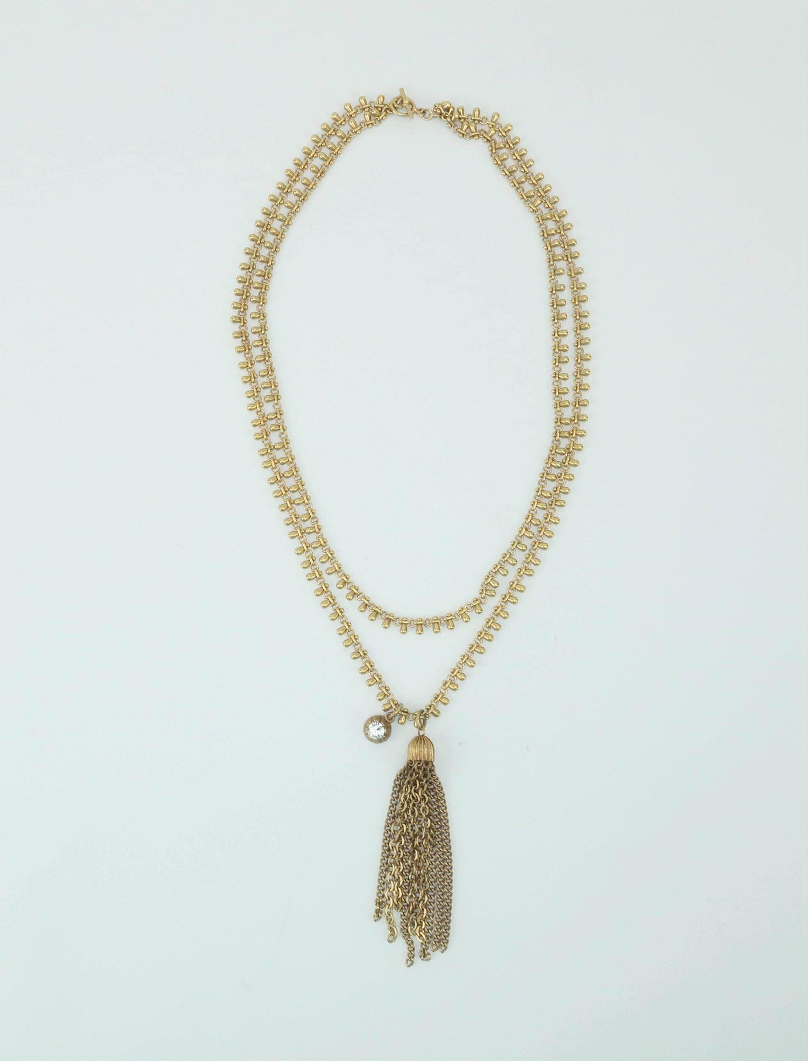 This vintage double stranded gold tone chain necklace begs for a closer look.  Each chain is formed by detailed articulated beading and serves to suspend a gold chain tassel and a single off-center crystal rhinestone pendant.  The overall effect of