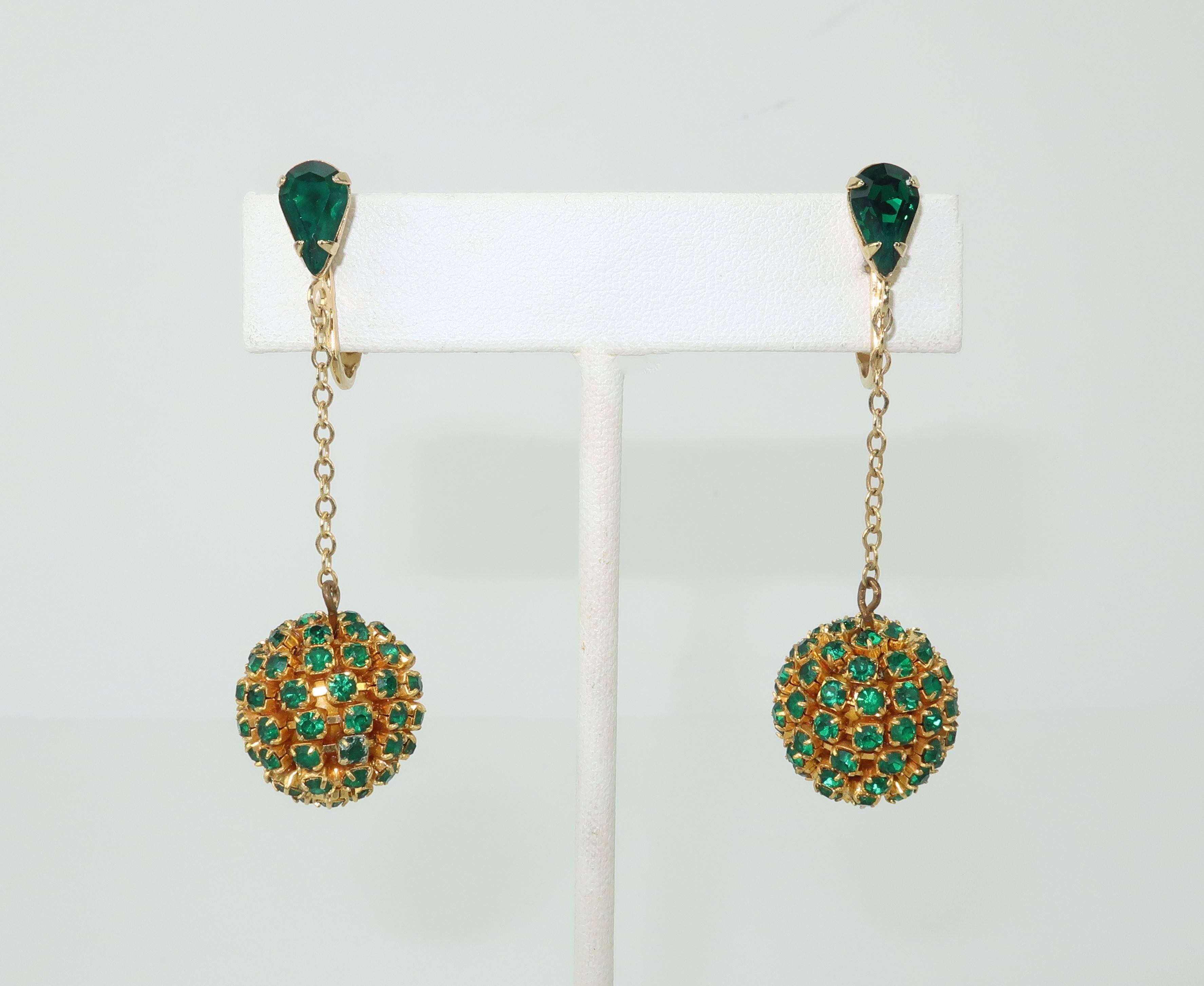 These delightful dangle earrings are akin to holiday ornaments for the ears.  Each earring consists of a gold tone orb fully encrusted with emerald green rhinestones suspended with a delicate chain attached to a teardrop shaped rhinestone base.  The