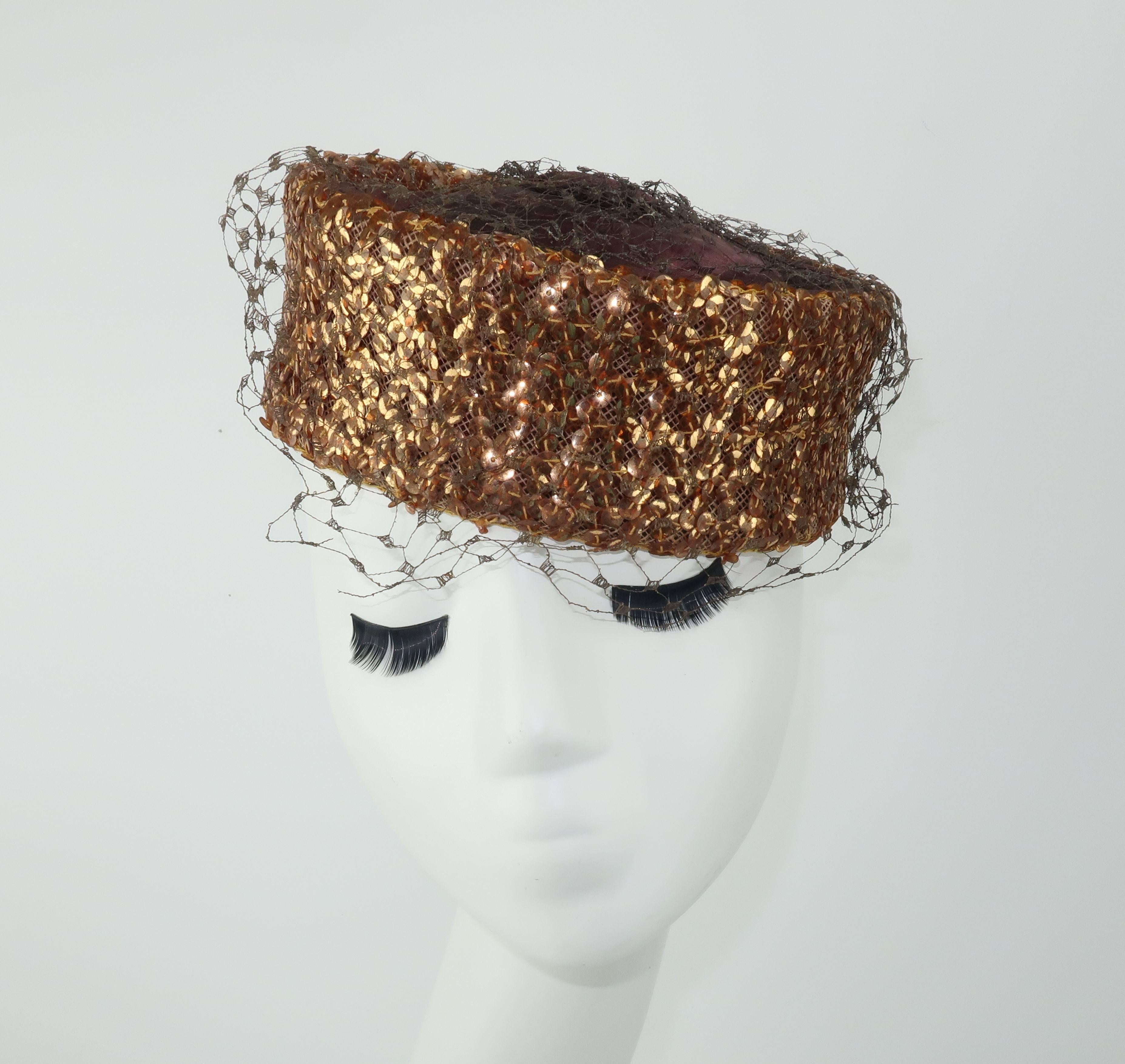 A glamorous topper is a fun way to add a vintage accessory to a modern day ensemble.  This classic brown satin pillbox hat is heavily embellished with copper sequins that catch the light in a dazzling way.  The button crown anchors a brown net and