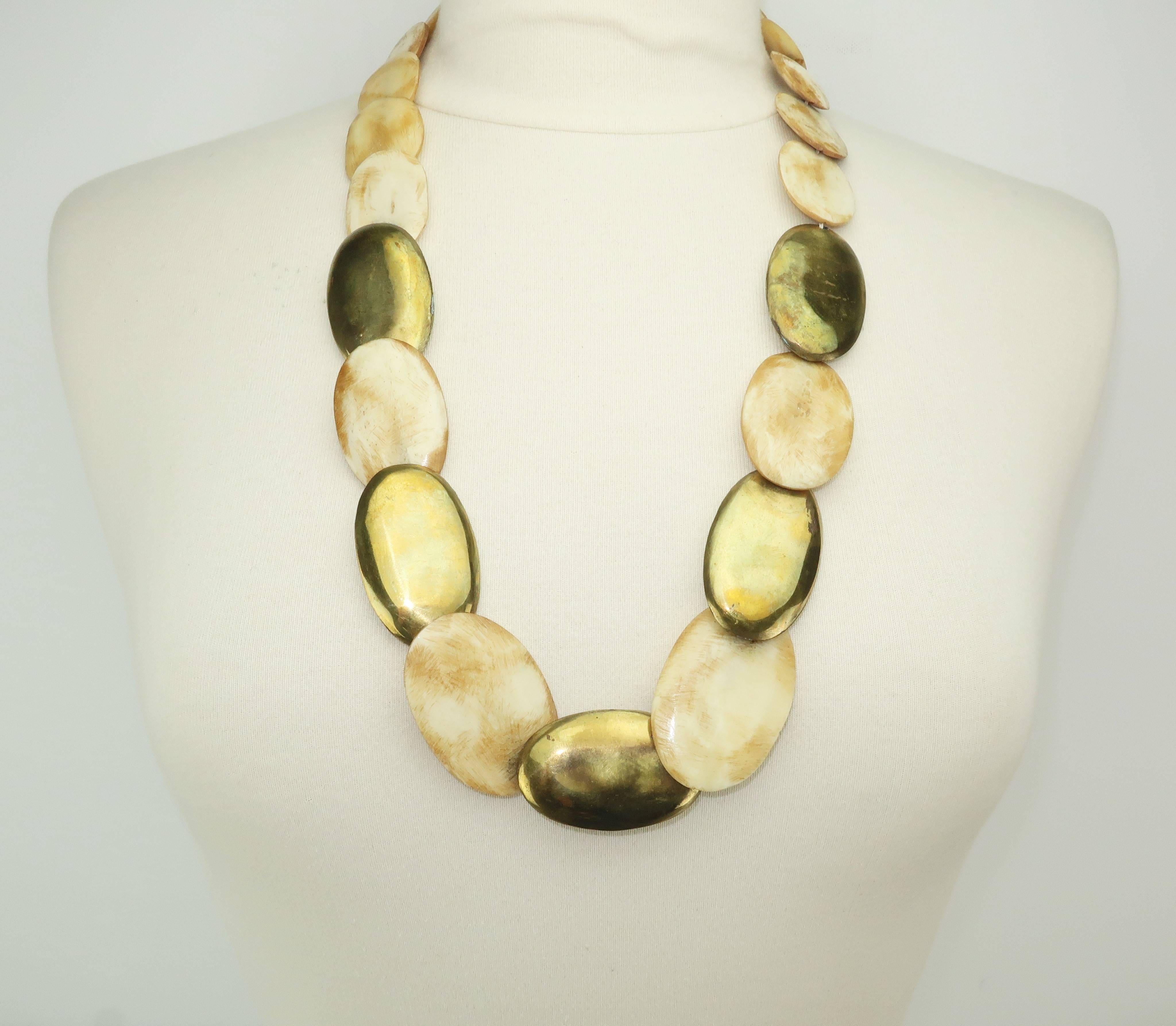 A touch of the exotic can transform a simple shift or t-shirt to a bohemian fashion statement.  This combination of bone and brass ovals are strung with graduated sizes to form a tribal style necklace that hooks at the back.  The ovals lay flat
