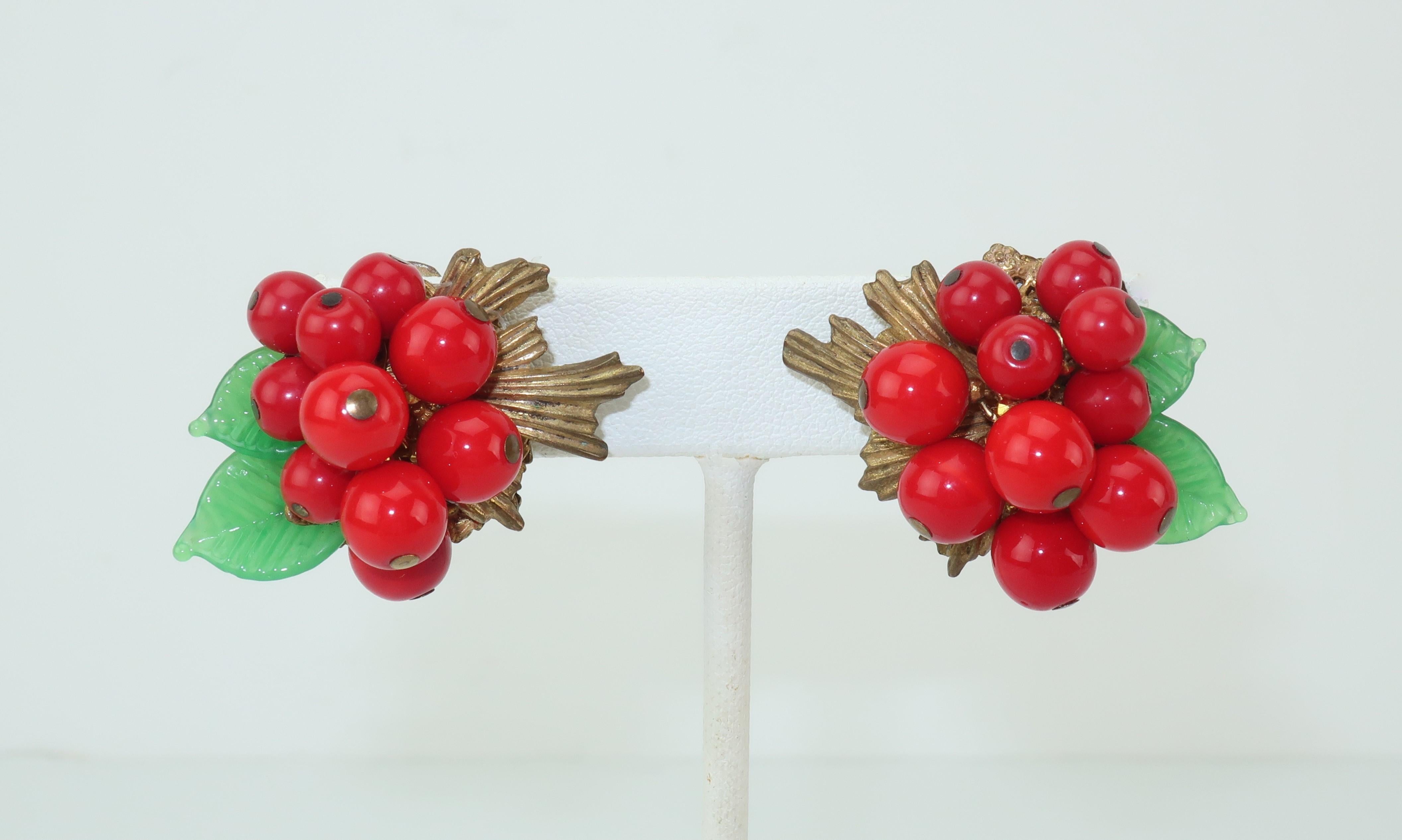 This 1950's Miriam Haskell demi parure, consisting of a brooch and clip on earrings, is reminiscent of holly berries with a vibrant combination of red glass beads and green glass leaves.  The wreath style brooch features 'berries' that dangle and