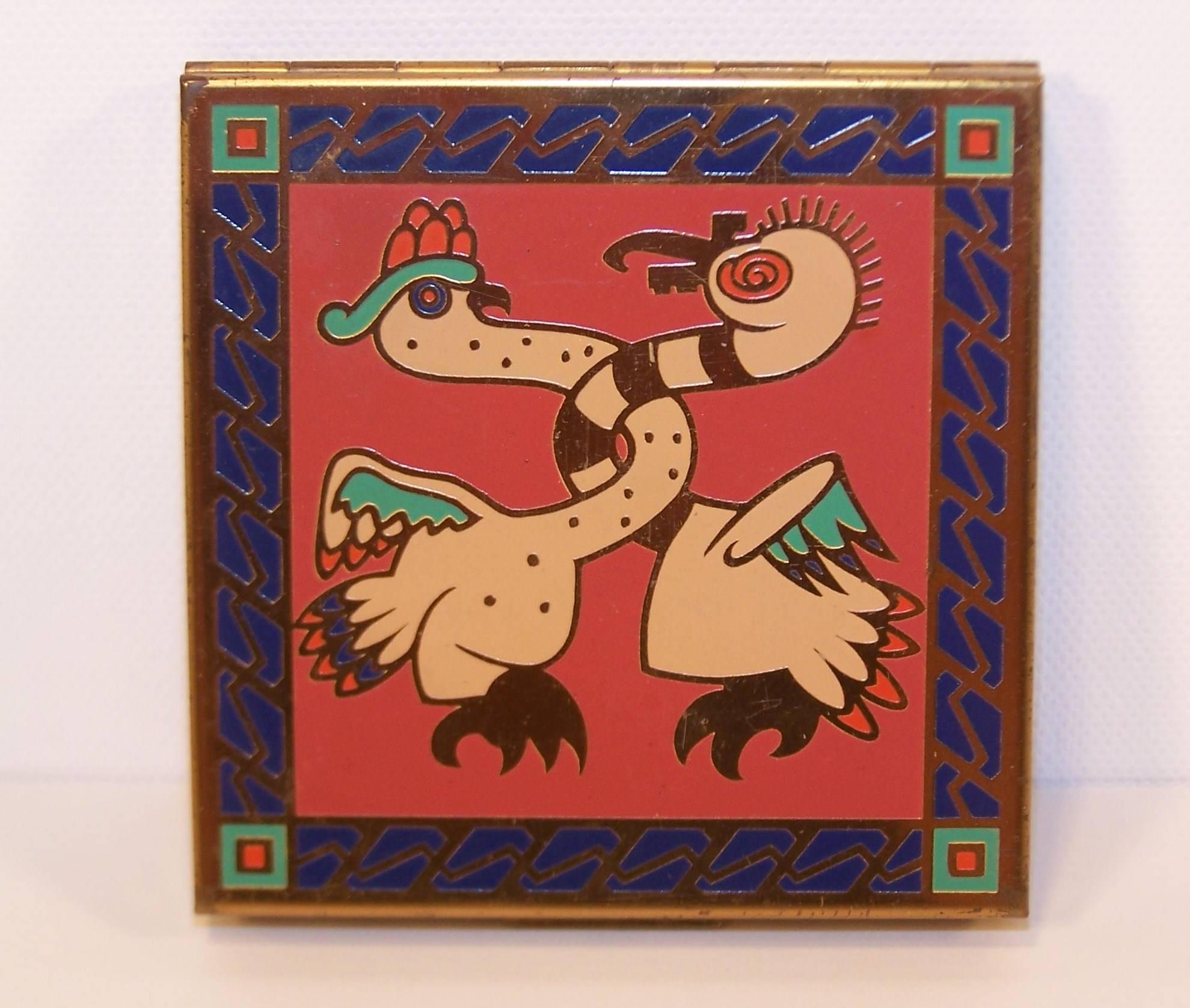 The graphic enameled decoration on this Zell mirrored compact is reminiscent of exotic pre-Columbian art or native American designs.  The chickens pictured on the front and back are outlined in gold with blue, green and red highlights.  The interior